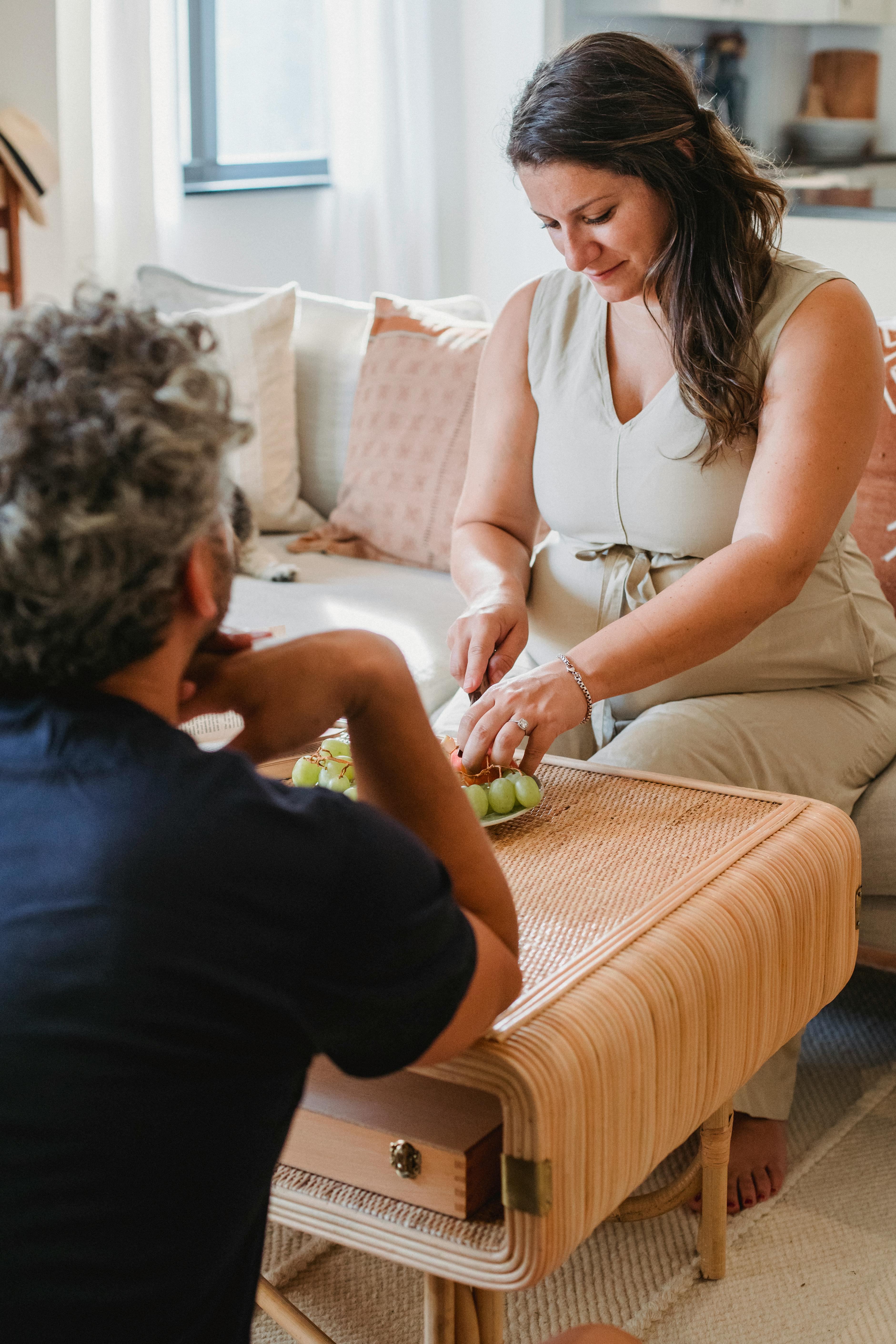 Hombre y mujer sentados en silencio mientras la mujer corta unas uvas | Fuente: Pexels