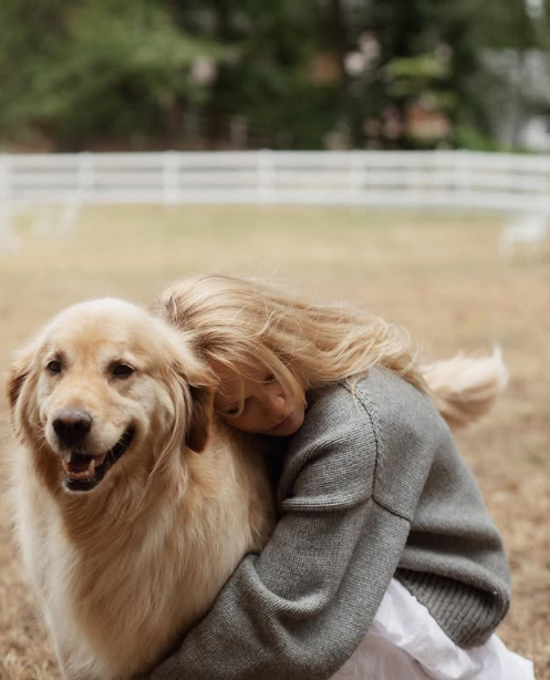 Pamela Anderson hunde la cara en el suave pelaje de su golden retriever durante un momento de tranquilidad al aire libre en su finca de Arcady. Abrigada con un jersey gris de punto grueso y una falda blanca vaporosa, con los árboles y la valla blanca del prado como telón de fondo, comparte un tierno abrazo que pone de manifiesto su profundo vínculo con los animales y la reconfortante sencillez de su hogar en la isla de Vancouver. Publicó esta conmovedora foto acompañada del siguiente pie de foto: "El amor verdadero nunca se acaba… 🤍". | Fuente: Instagram/pamelaanderson