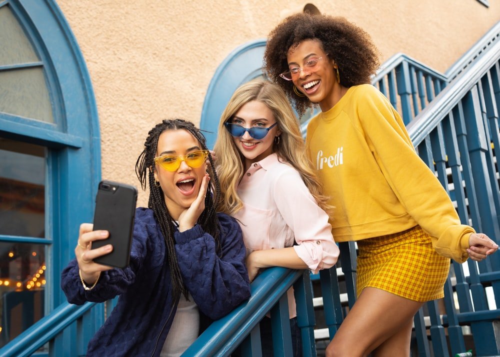 Tres chicas sacándose fotos con un teléfono celular. | Foto: Unsplash 