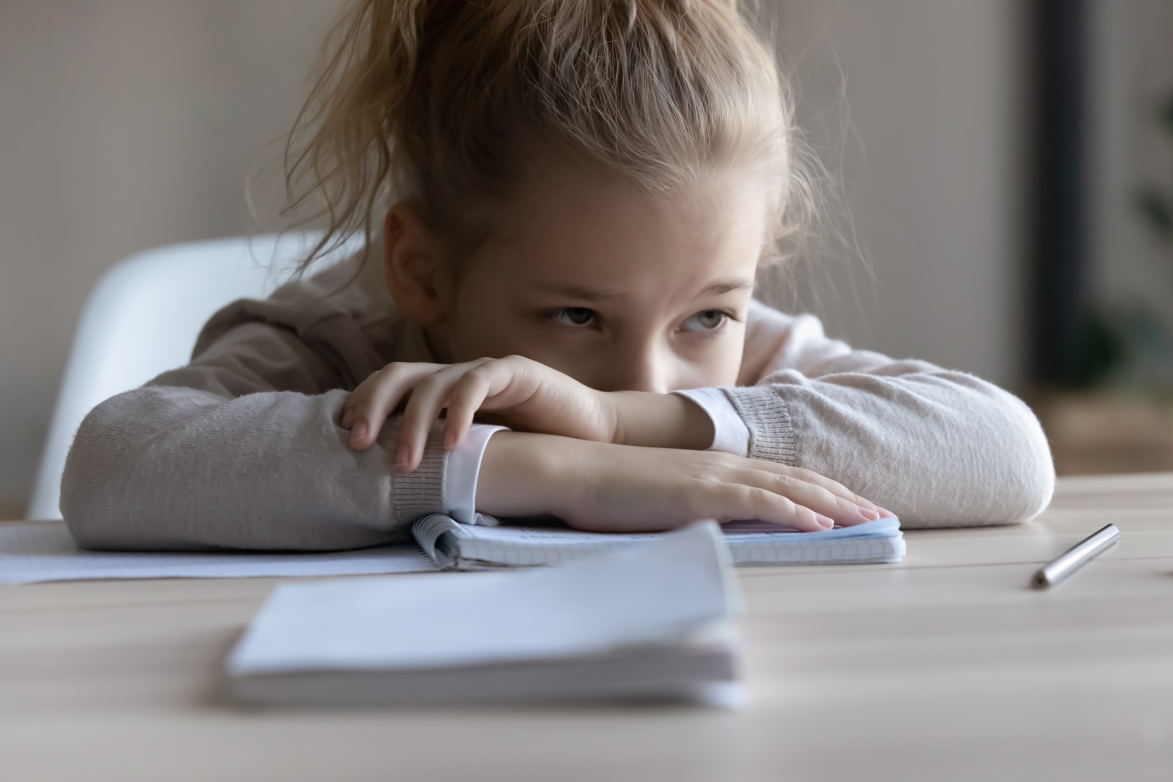 Una niña triste apoya la cabeza en el escritorio, distraída del trabajo. | Foto: Shutterstock