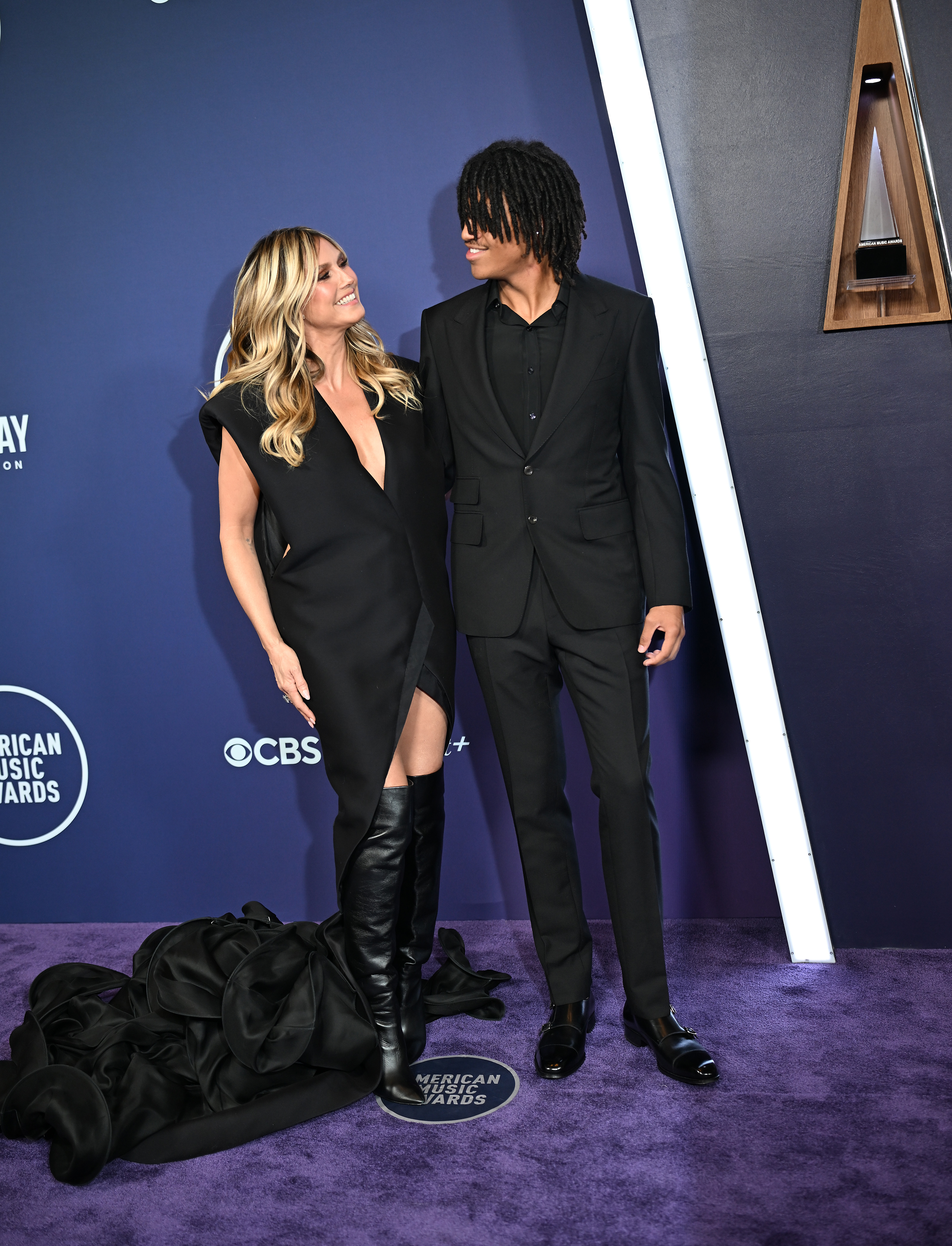 Heidi Klum comparte un cálido momento con su hijo, Henry Samuel, mientras intercambian sonrisas en la alfombra roja de los AMAs - la espectacular cola de ella junto a su elegante traje negro.