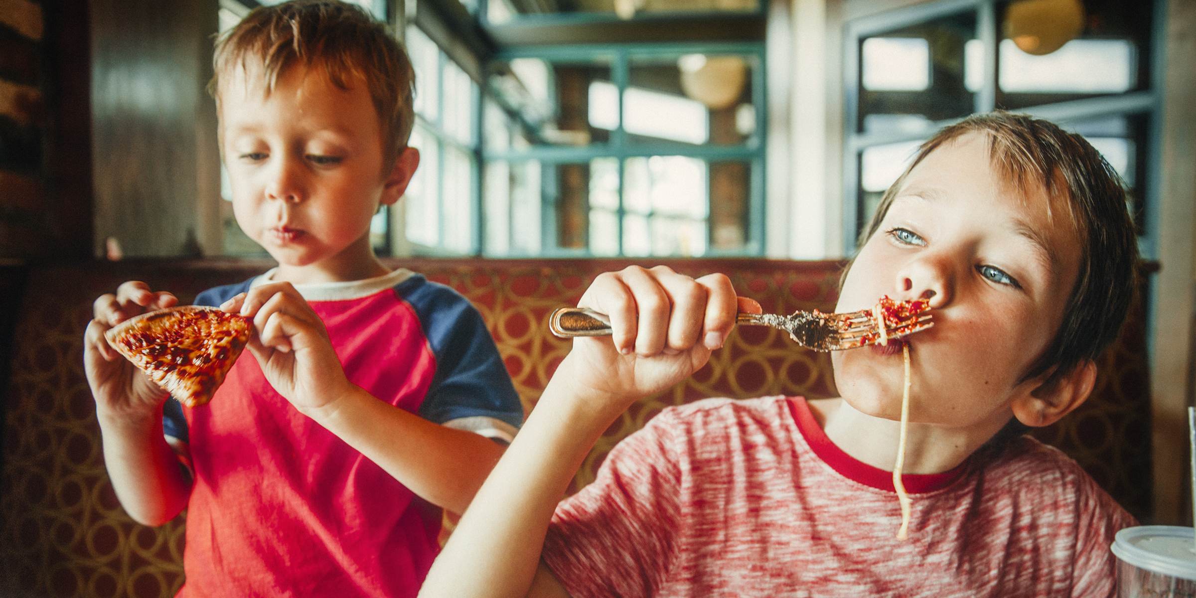 Dos niños comiendo pizza y pasta en un restaurante | Fuente: Shutterstock