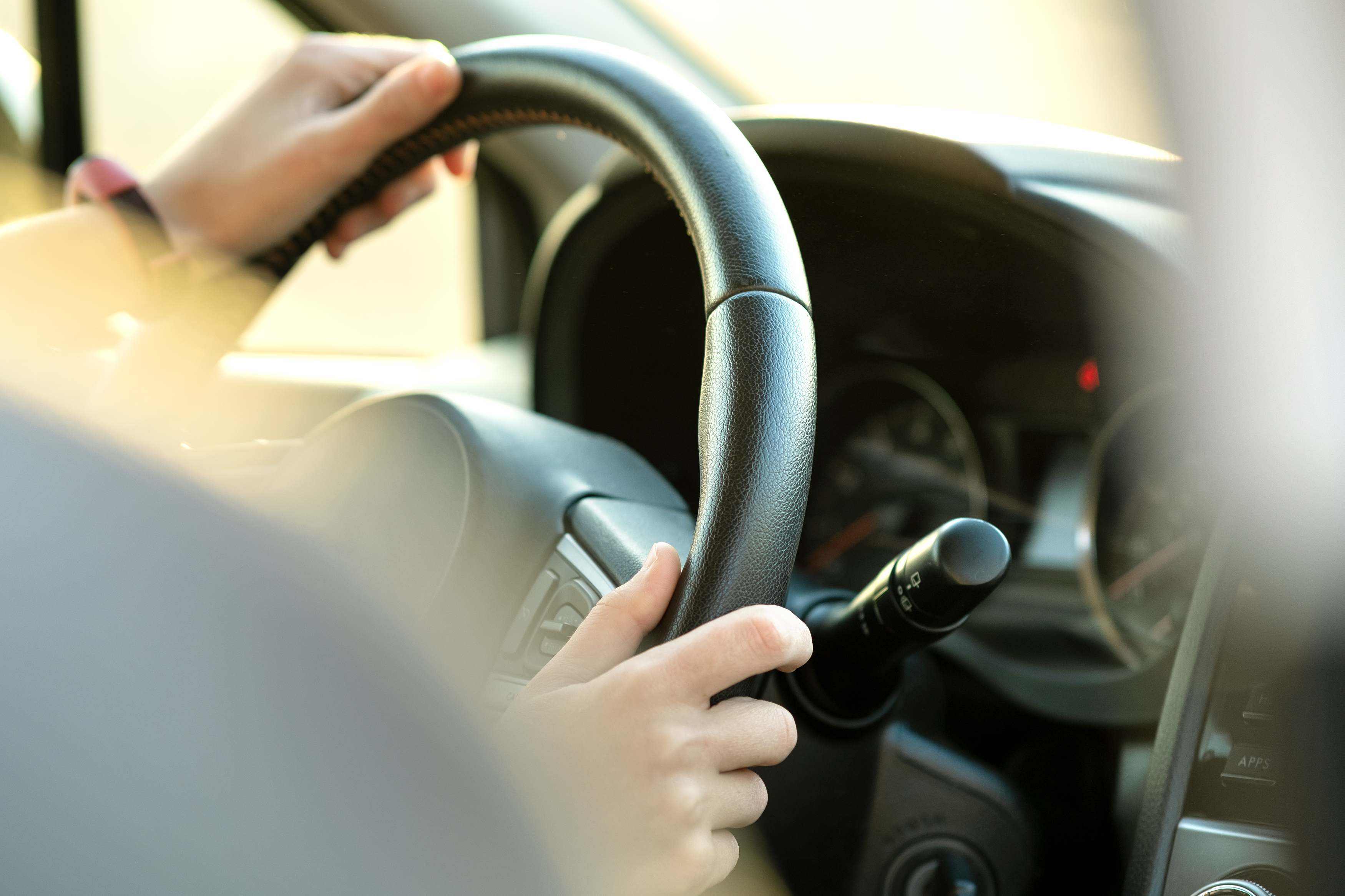 Primer plano de las manos de una mujer sujetando el volante conduciendo un Automóvil en una calle de la ciudad en un día soleado. | Fuente: Shutterstock