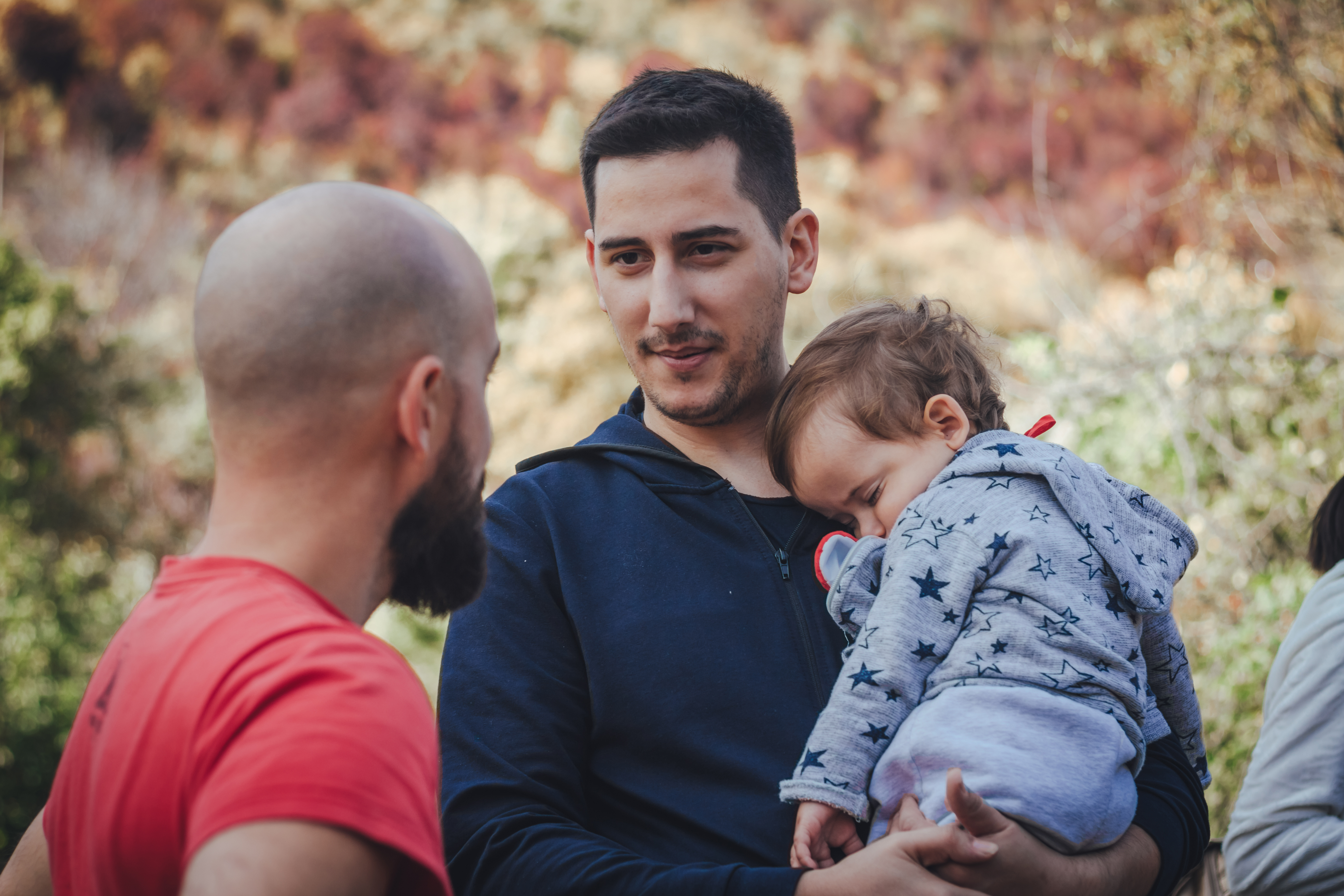 Dos hombres hablando y uno de ellos con un bebé en brazos | Foto: Shutterstock