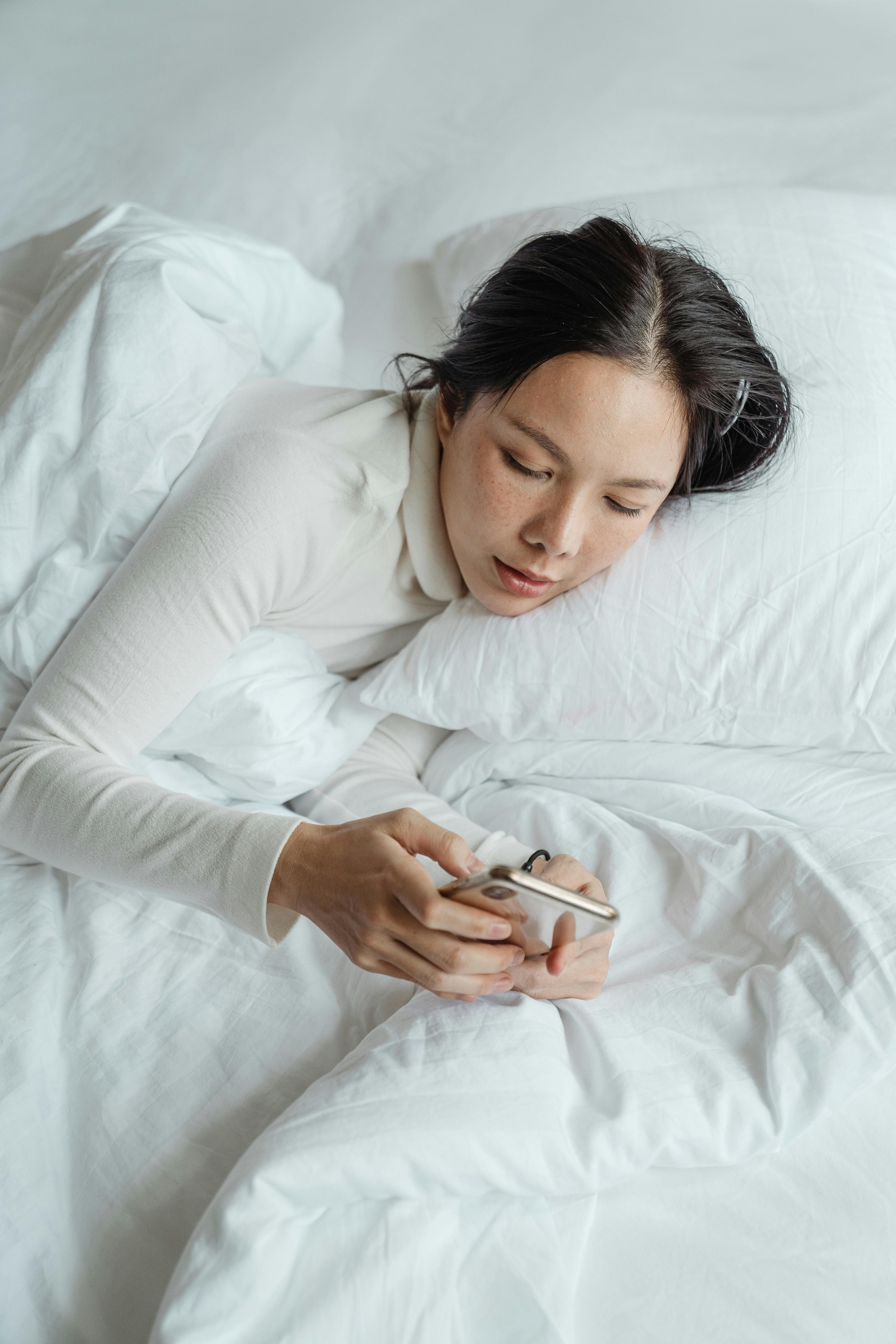 Una mujer escribiendo en su teléfono mientras está tumbada en la cama | Fuente: Pexels