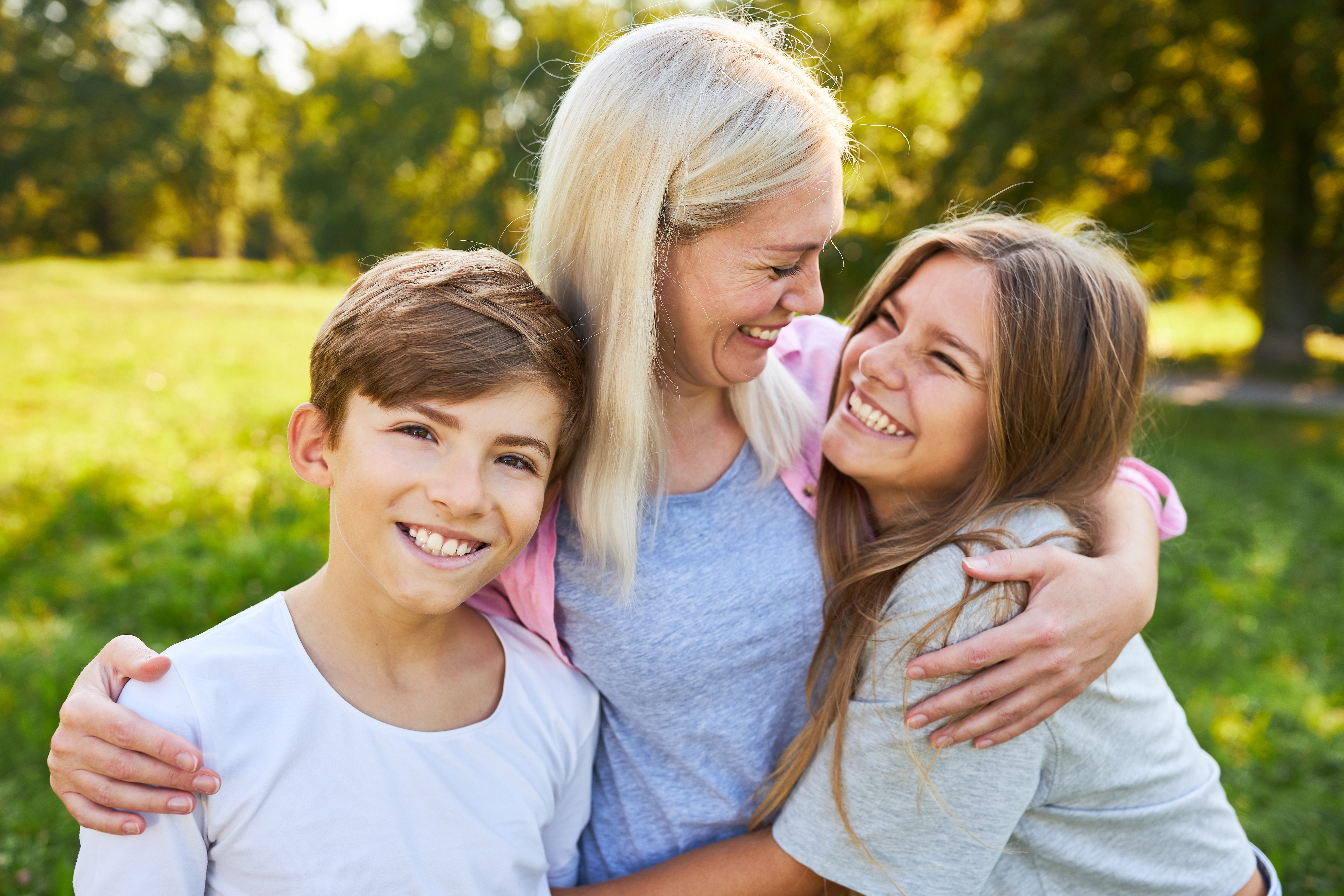 Una madre feliz abrazando a sus dos hijos al aire libre | Foto: Shutterstock