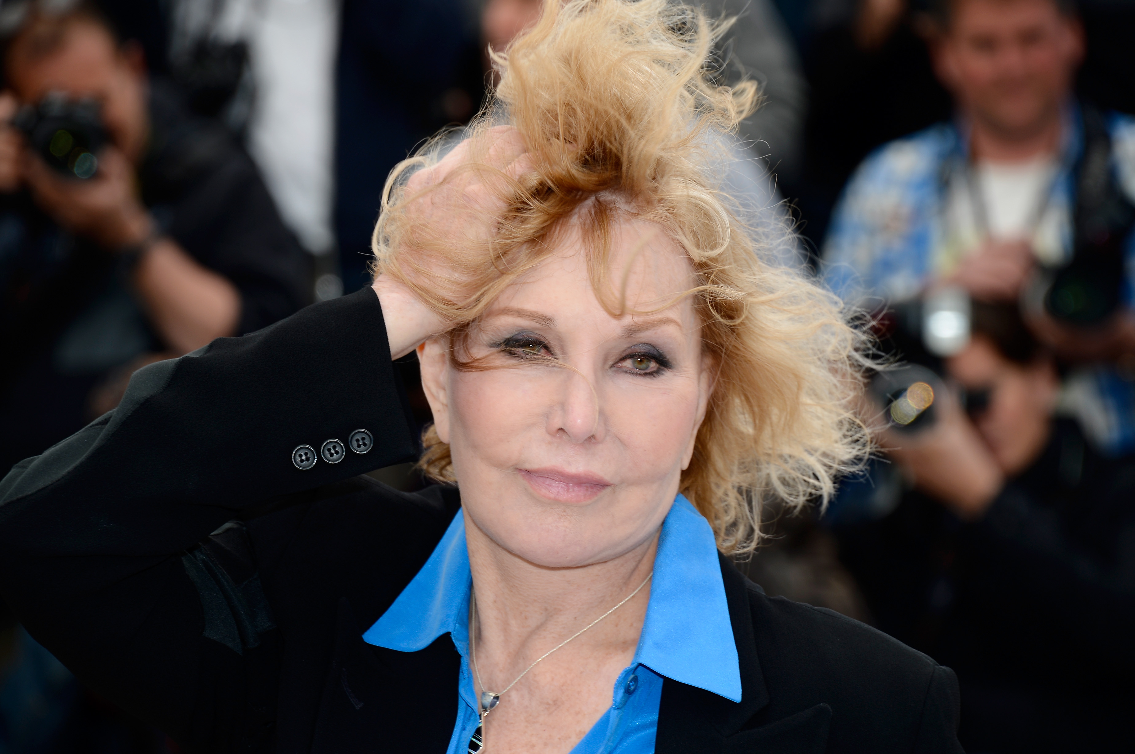Kim Novak se arregla el pelo mientras posa para los fotógrafos en el Festival de Cine de Cannes, en mayo de 2013, con una chaqueta negra y una camisa azul brillante. | Fuente: Getty Images