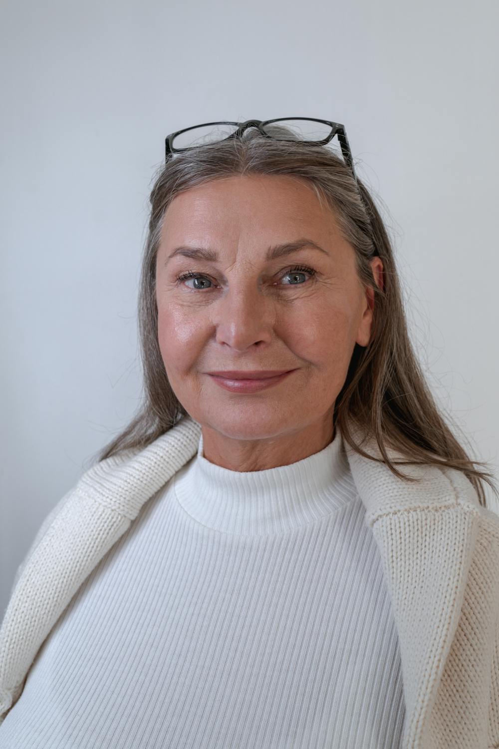 Una mujer sonriente con un jersey blanco ⏐ Fuente: Pexels