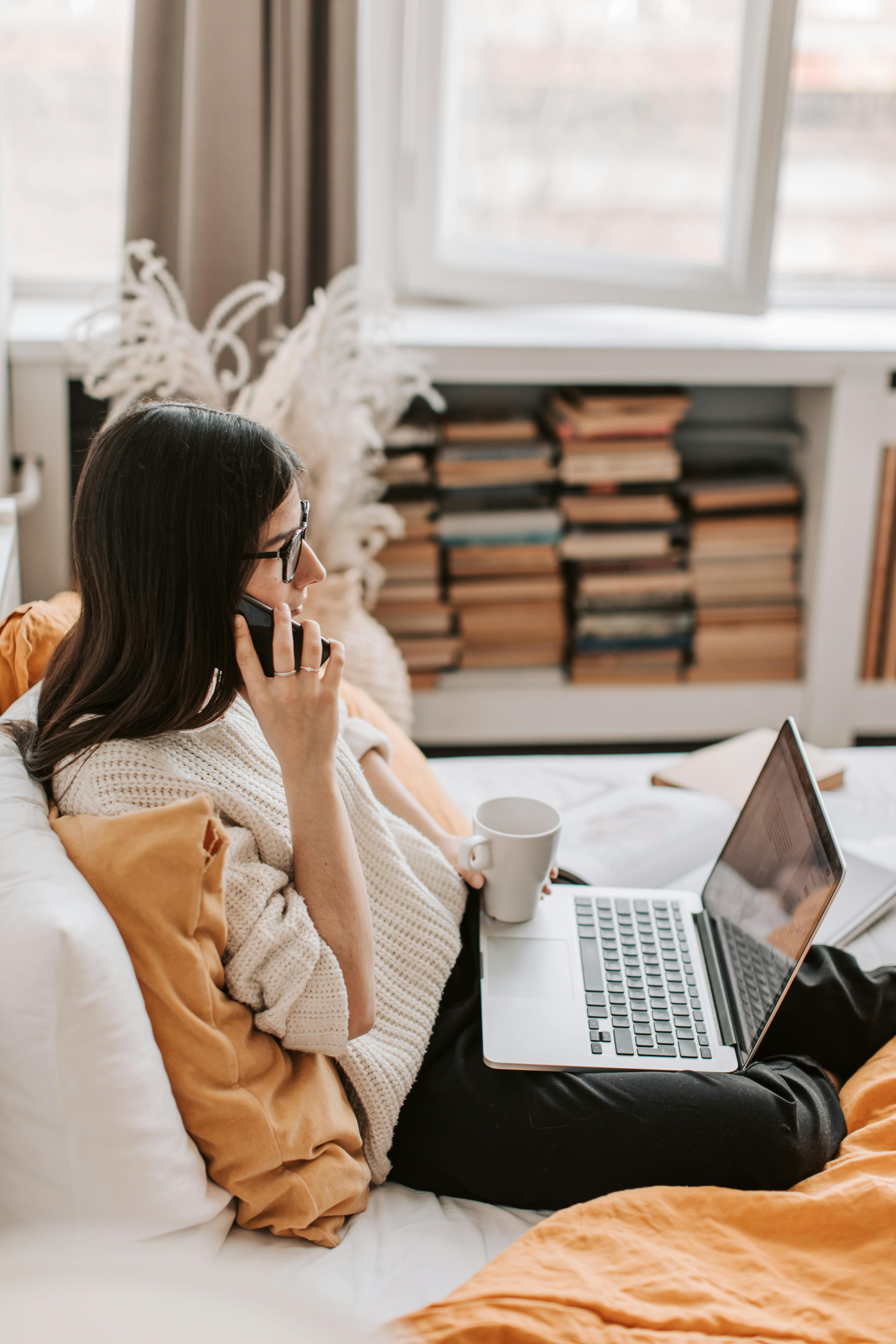 Una mujer hablando por teléfono en casa, con su portátil delante | Fuente: Pexels