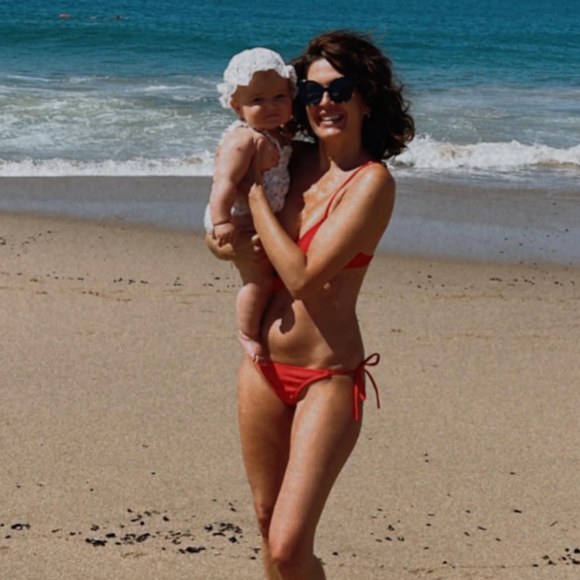 Isabel Macedo en la playa sosteniendo a su hija menor Julia en brazos cuando era una bebé | Fuente: Instagram/isabelmacedophoto