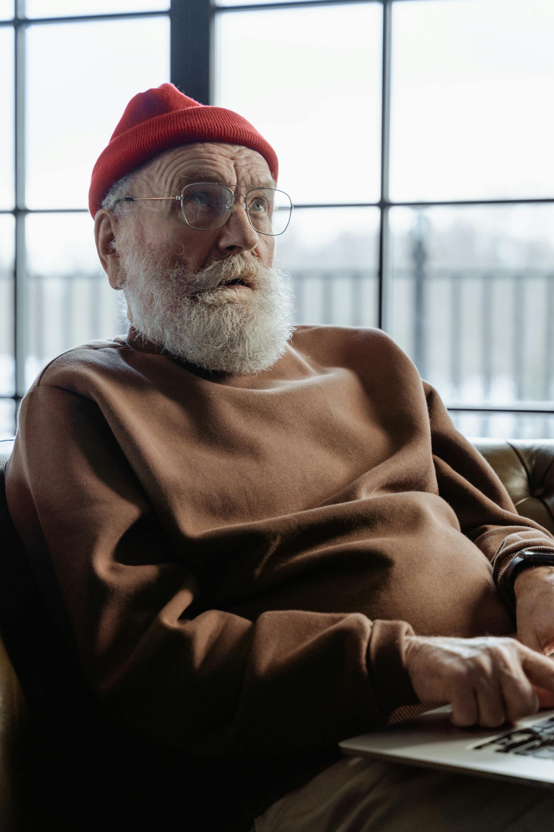 Un hombre mayor con un gorro rojo sentado en una silla y mirando a alguien | Fuente: Pexels