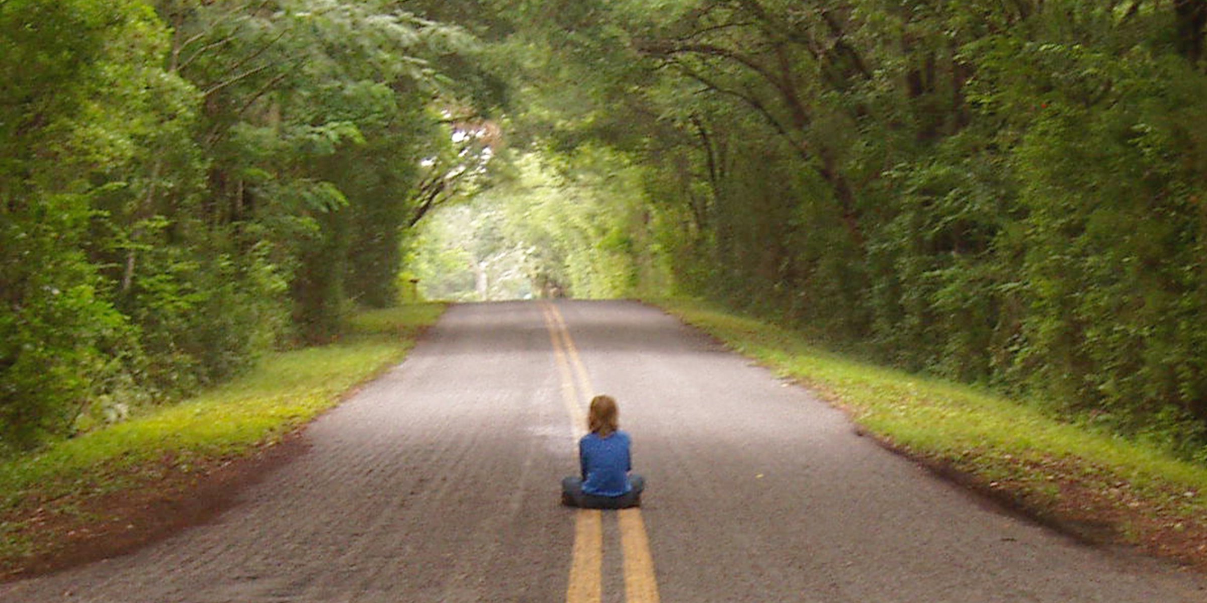 Un niño sentado en medio de un camino rodeado de árboles | Foto: Shutterstock