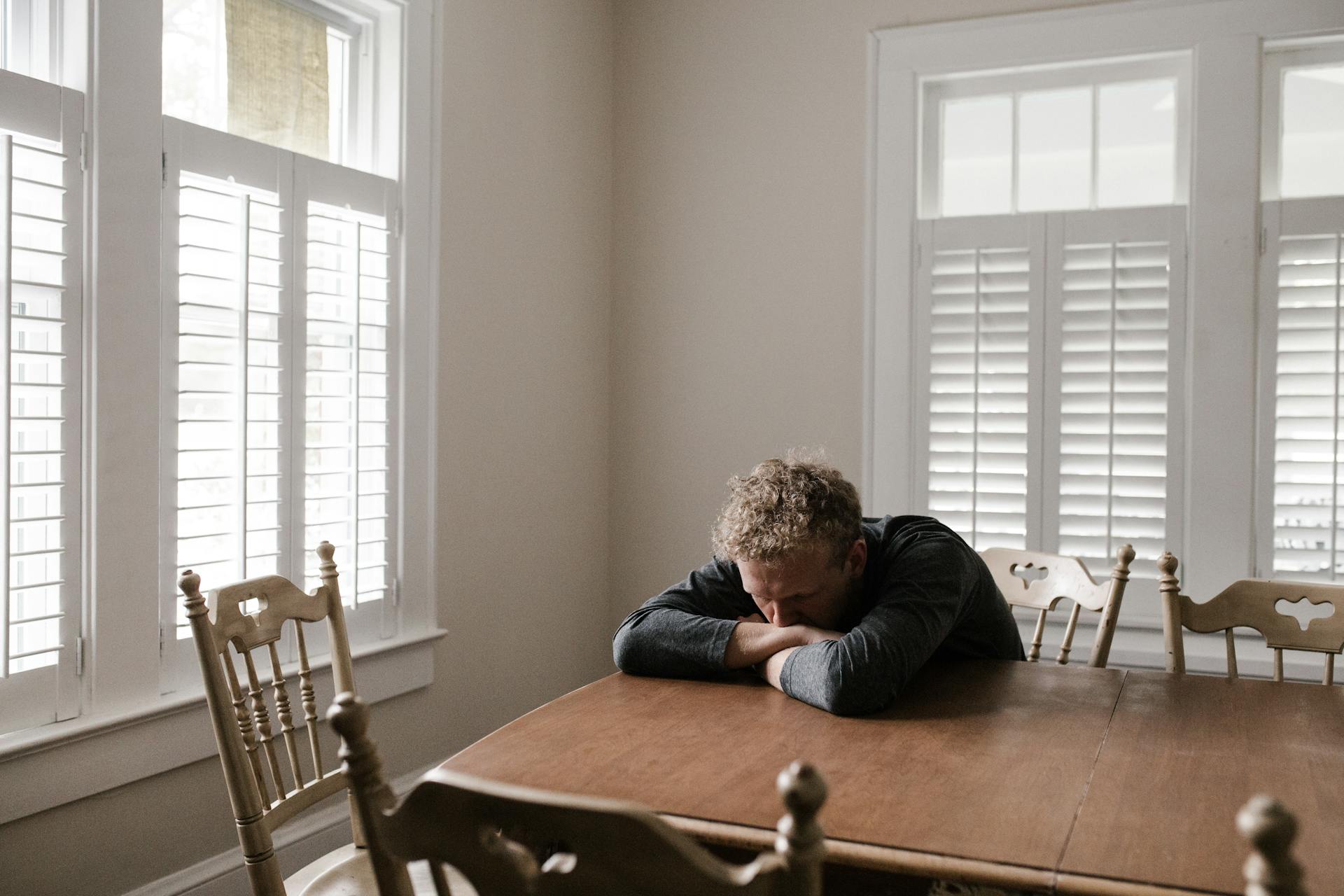 Un hombre preocupado apoyado en una mesa de madera marrón | Fuente: Pexels