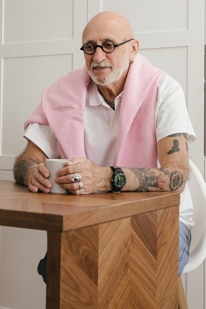 Un hombre mayor con tatuajes toma una taza entre sus manos. | Foto: Pexels