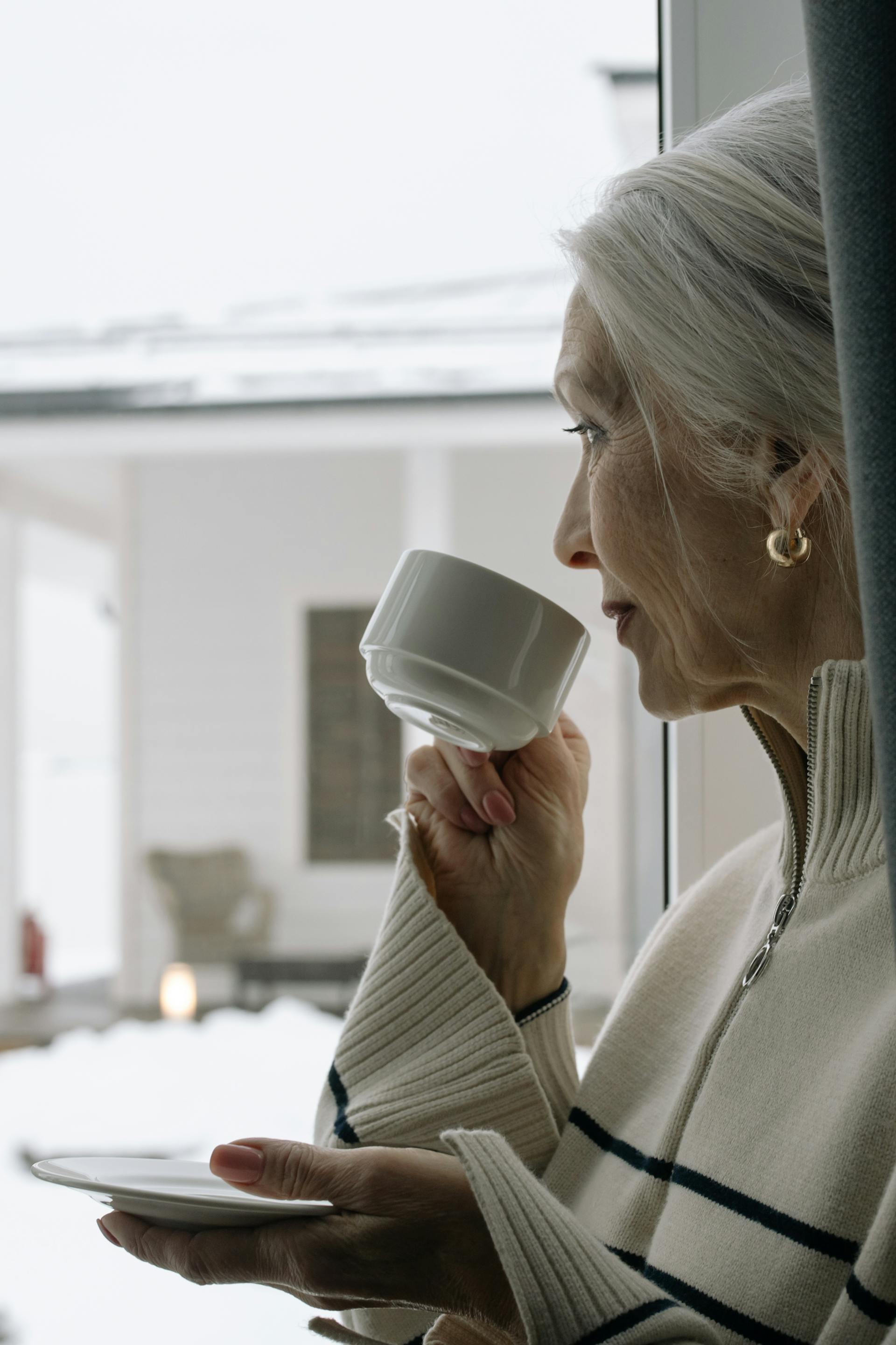 Una mujer sonriendo débilmente mientras mira por una ventana | Fuente: Pexels