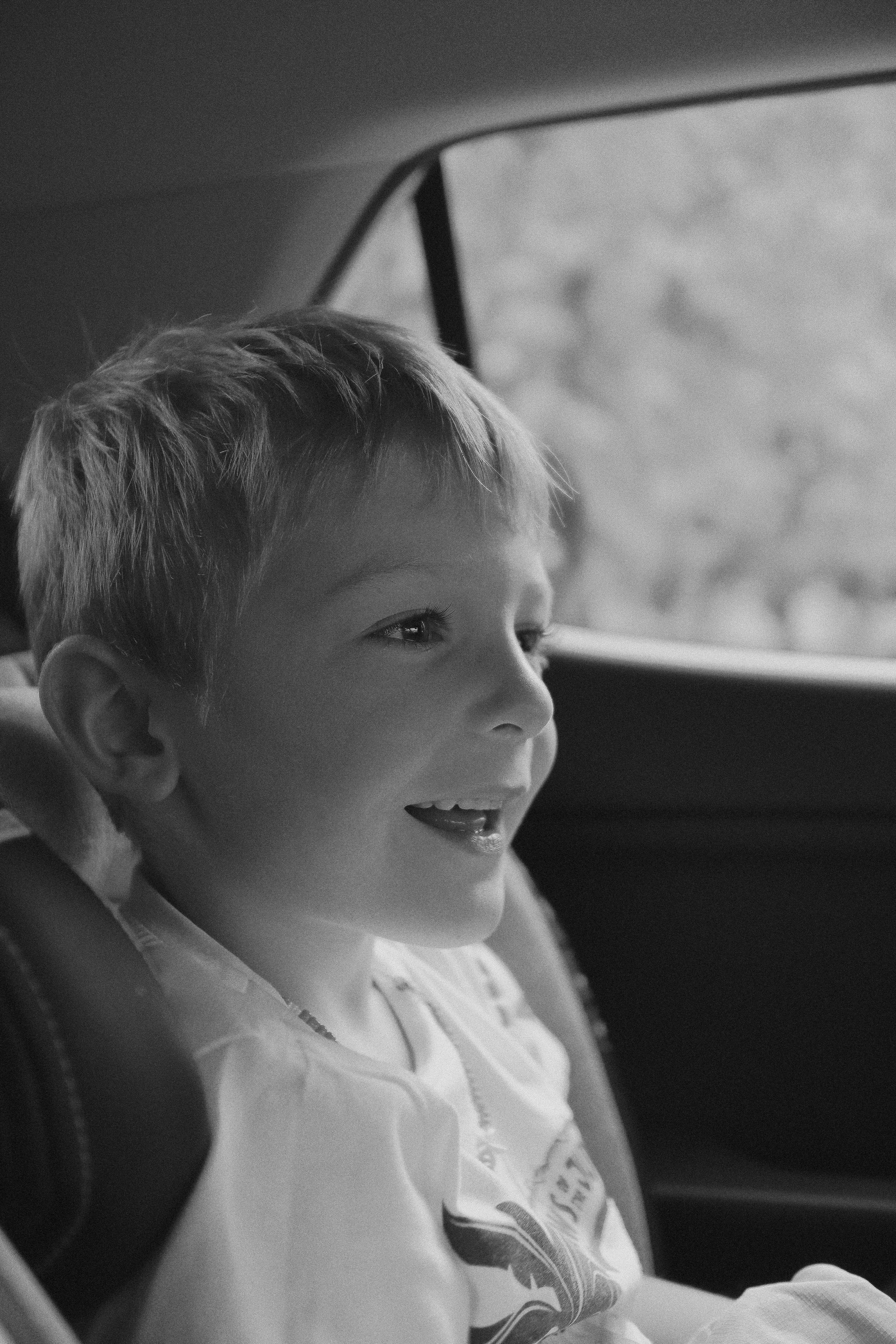 Foto en escala de grises de un niño sentado en el asiento trasero de un automóvil | Fuente: Unsplash