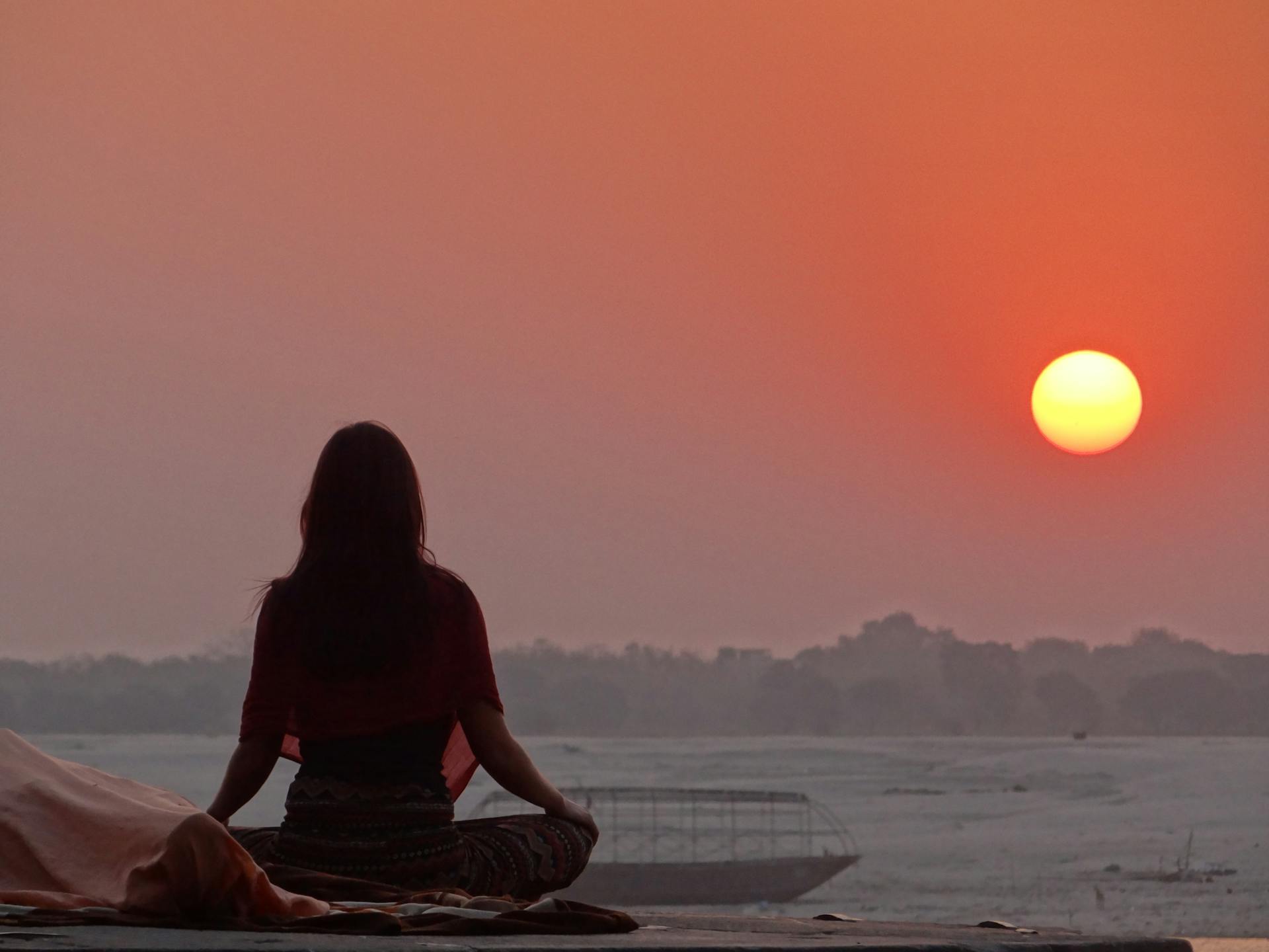 Una mujer meditando cerca del mar al atardecer | Fuente: Pexels