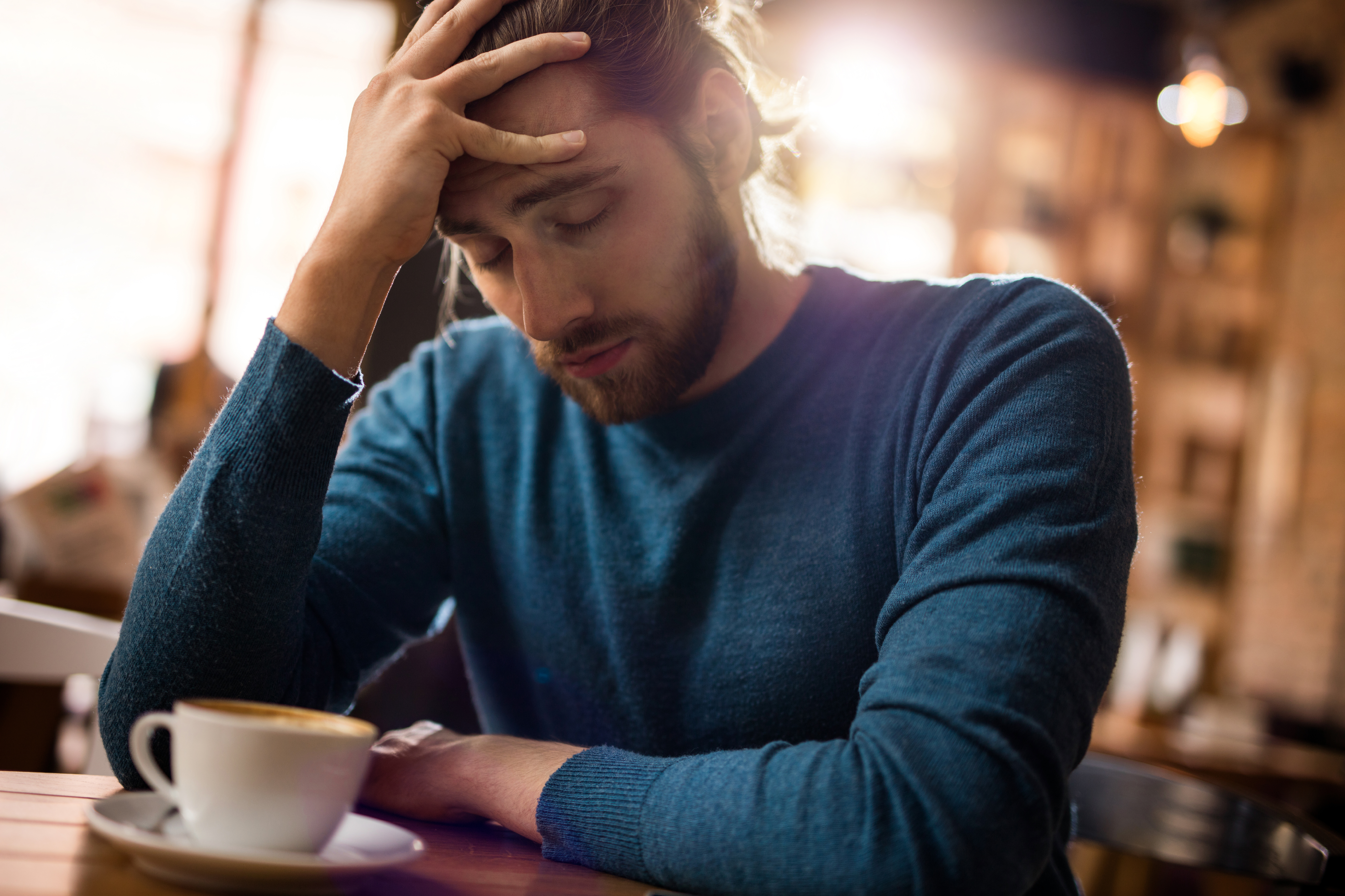 Hombre estresado sujetándose la cabeza por el dolor en una cafetería | Foto: Getty Images