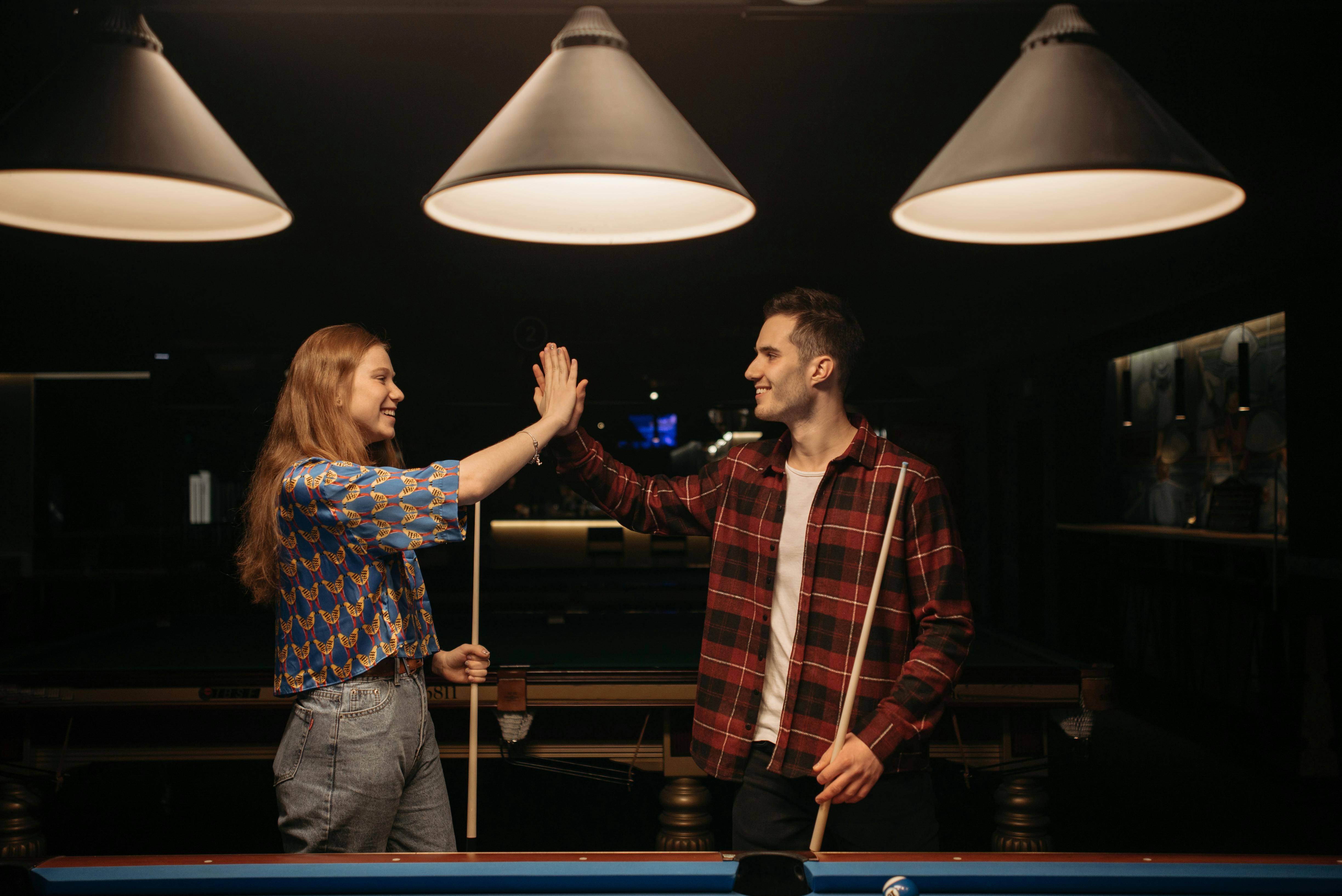 Un hombre y una mujer chocando los cinco cerca de una mesa de billar | Fuente: Pexels