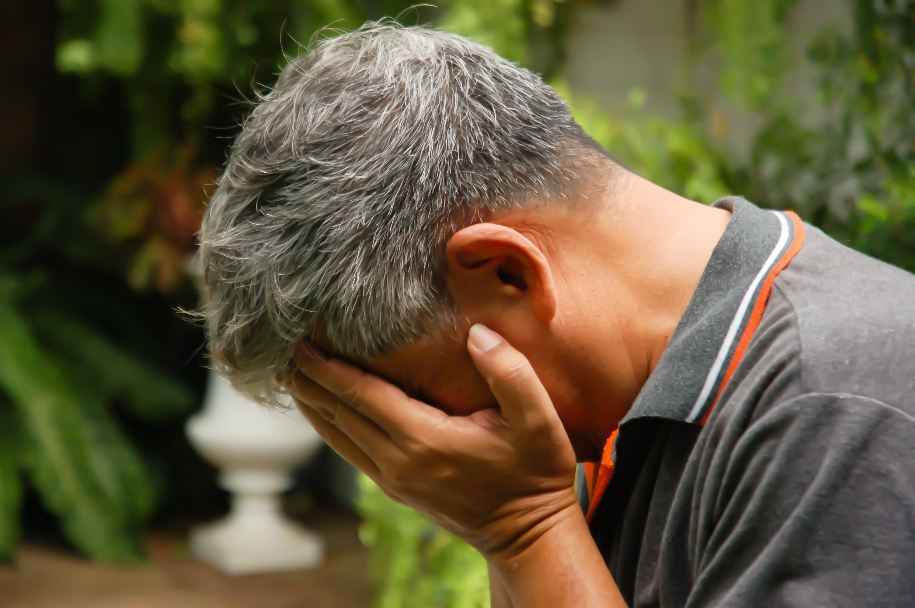 Un anciano deprimido cubriéndose la cara con las manos | Fuente: Shutterstock