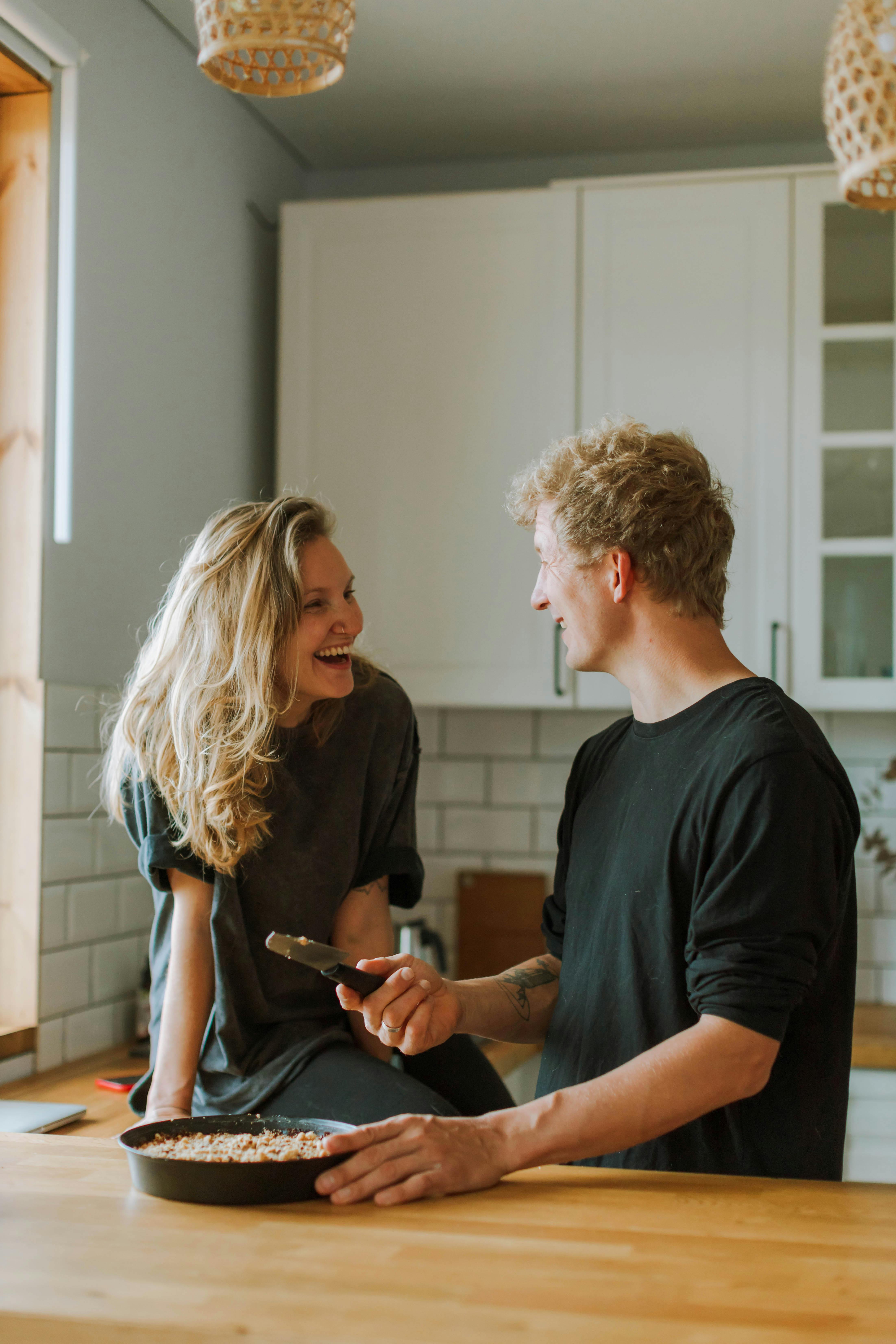 Hombre y mujer riendo mientras preparan una comida en la cocina | Fuente: Pexels