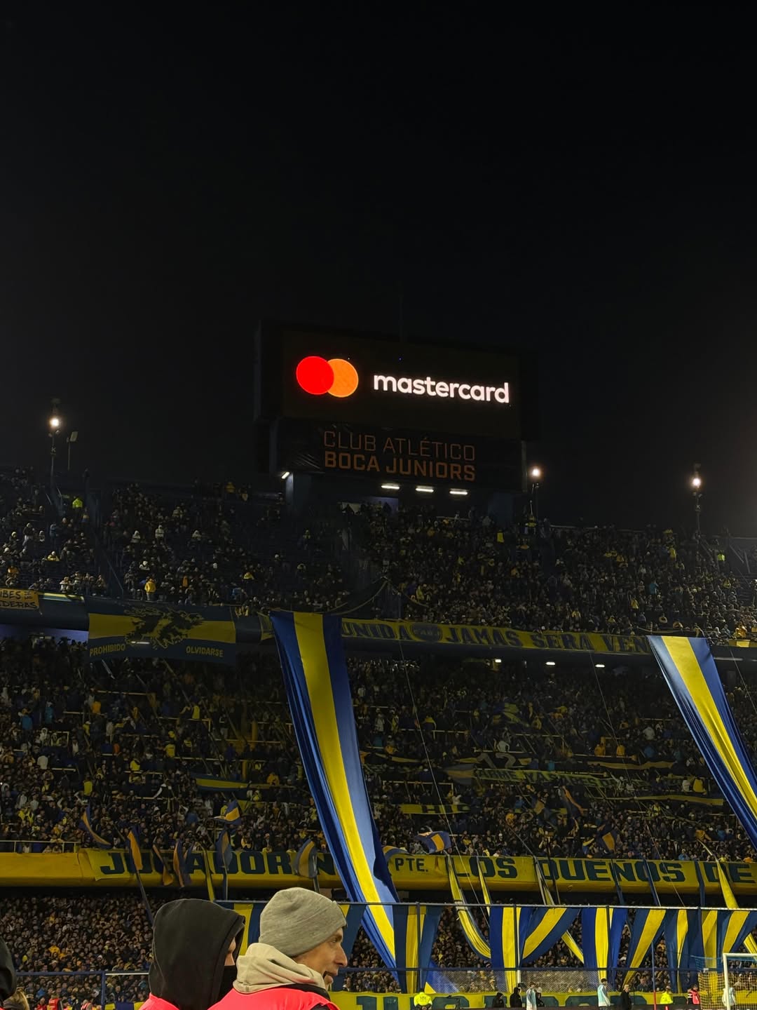 Vista nocturna de las tribunas de La Bombonera colmadas de hinchas de Boca Juniors con banderas azul y amarillo durante el partido. | Fuente: Instagram/zaira.nara