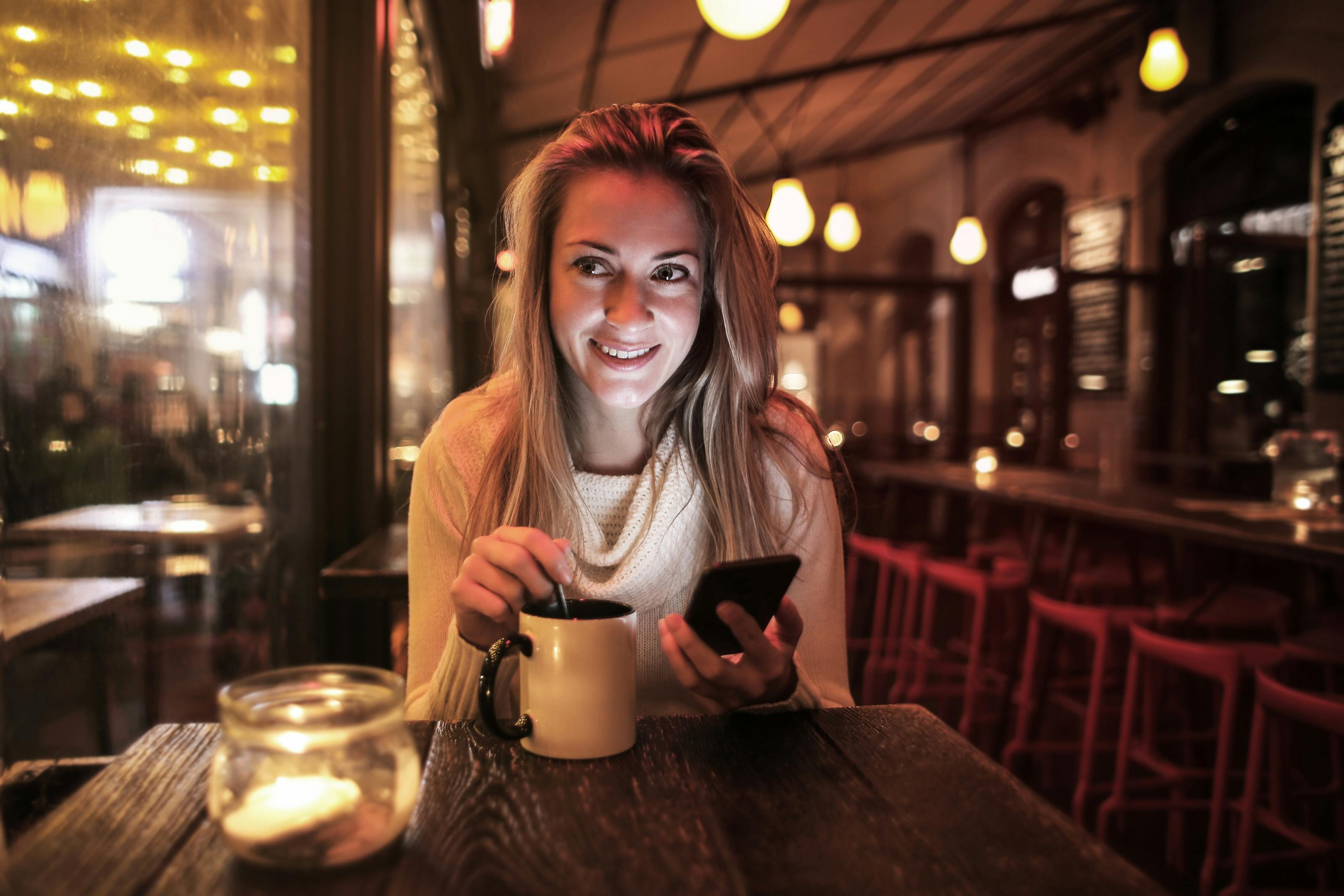 Una mujer sujetando su teléfono en una cafetería | Fuente: Pexels