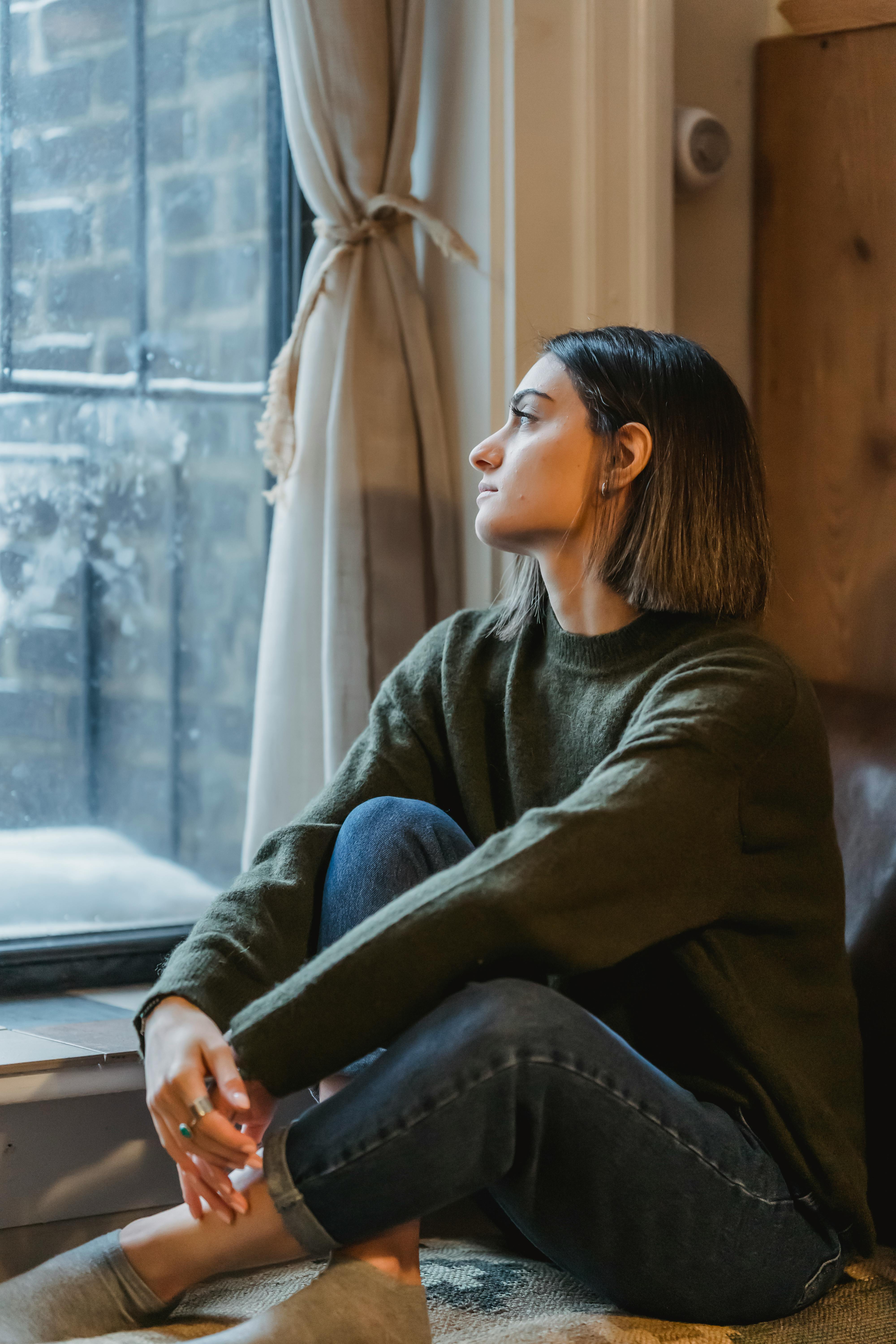 Una joven mirando pensativamente por una ventana | Fuente: Pexels