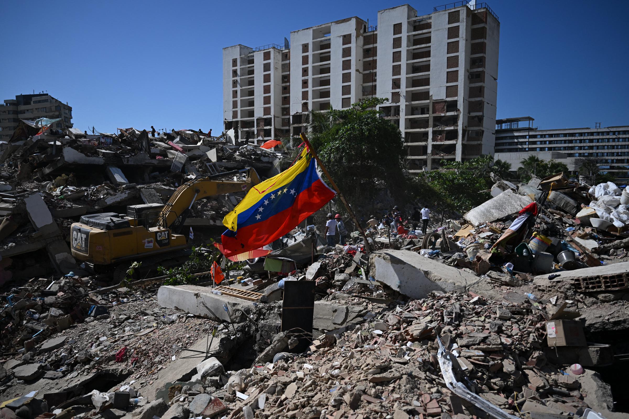 Una bandera venezolana ondea mientras una retroexcavadora retira escombros en Caraballeda, estado de La Guaira, Venezuela, el 7 de julio de 2026, tras los terremotos que azotaron la región. | Fuente: Getty Images