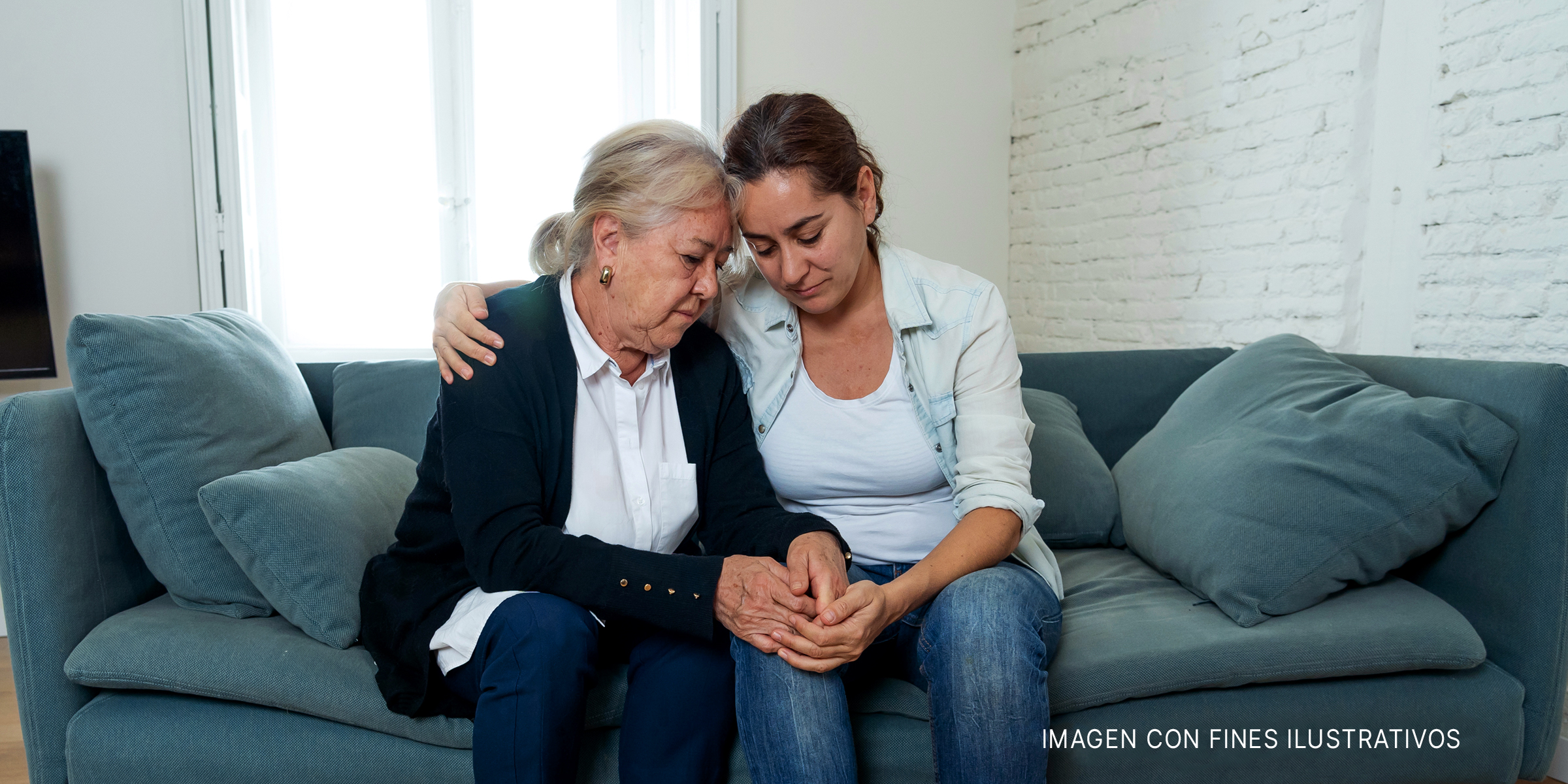 Mujer mayor y mujer más joven abrazadas en un sofá. | Foto: Shutterstock