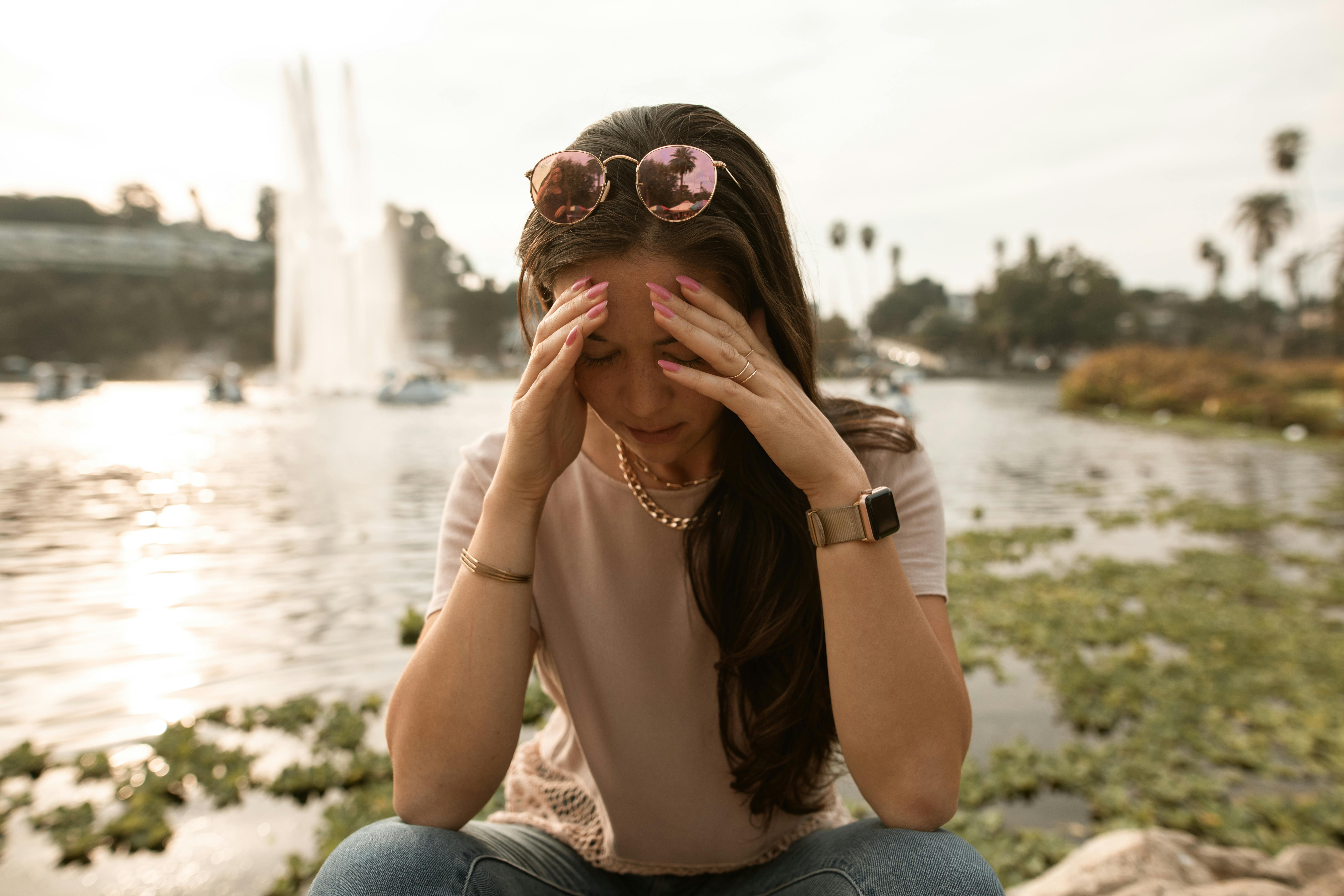 Una mujer angustiada sentada a la orilla de un lago y tocándose la cara con desesperación | Fuente: Pexels