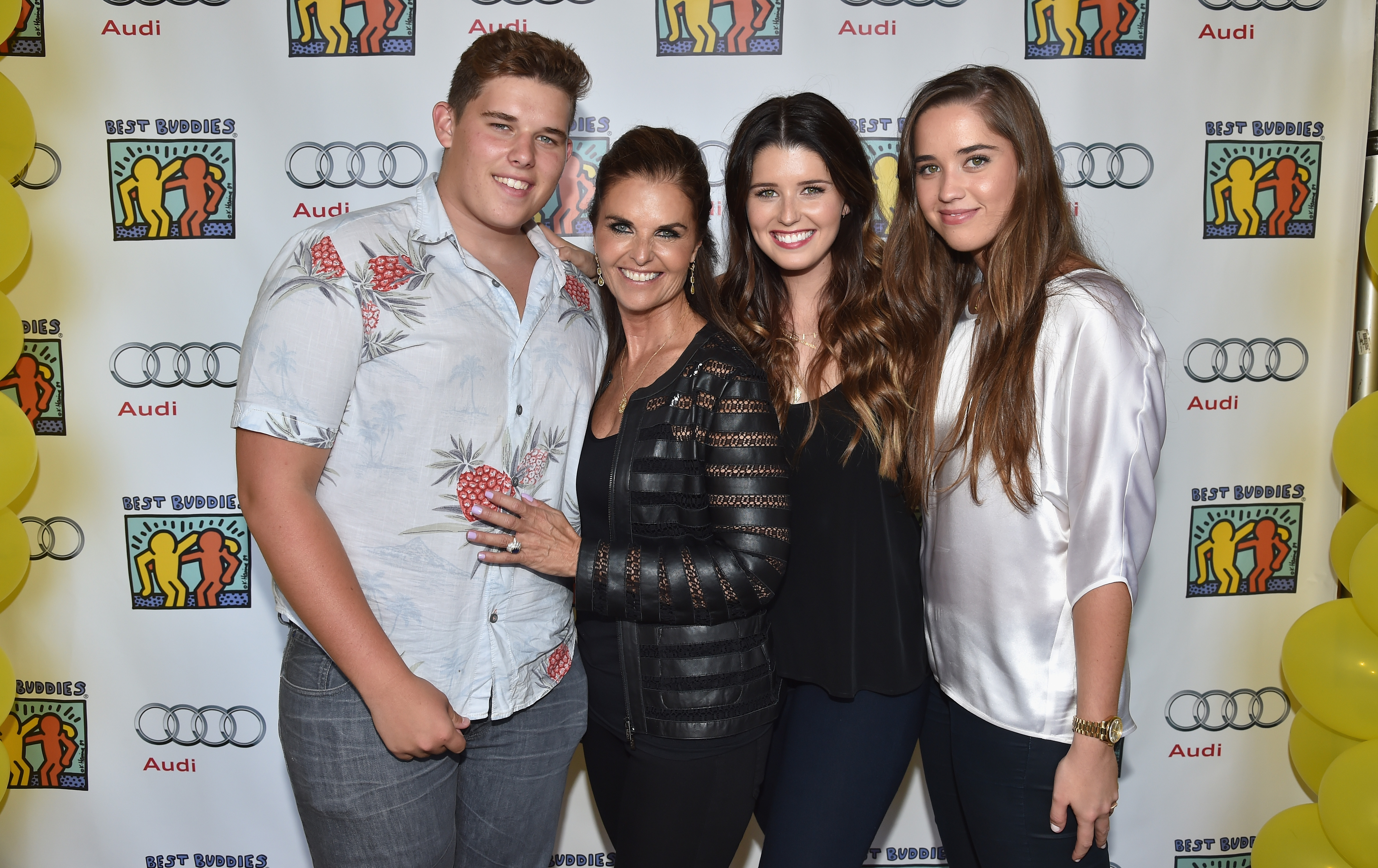 Christopher posa con su madre, Maria Shriver, y sus hermanas Katherine y Christina en un acto en Beverly Hills. Lleva una camisa ligera abotonada con un llamativo estampado de frutas y vaqueros grises, y posa sonriente y seguro de sí mismo, con el pelo corto bien peinado y una complexión visiblemente más rellena en ese momento.