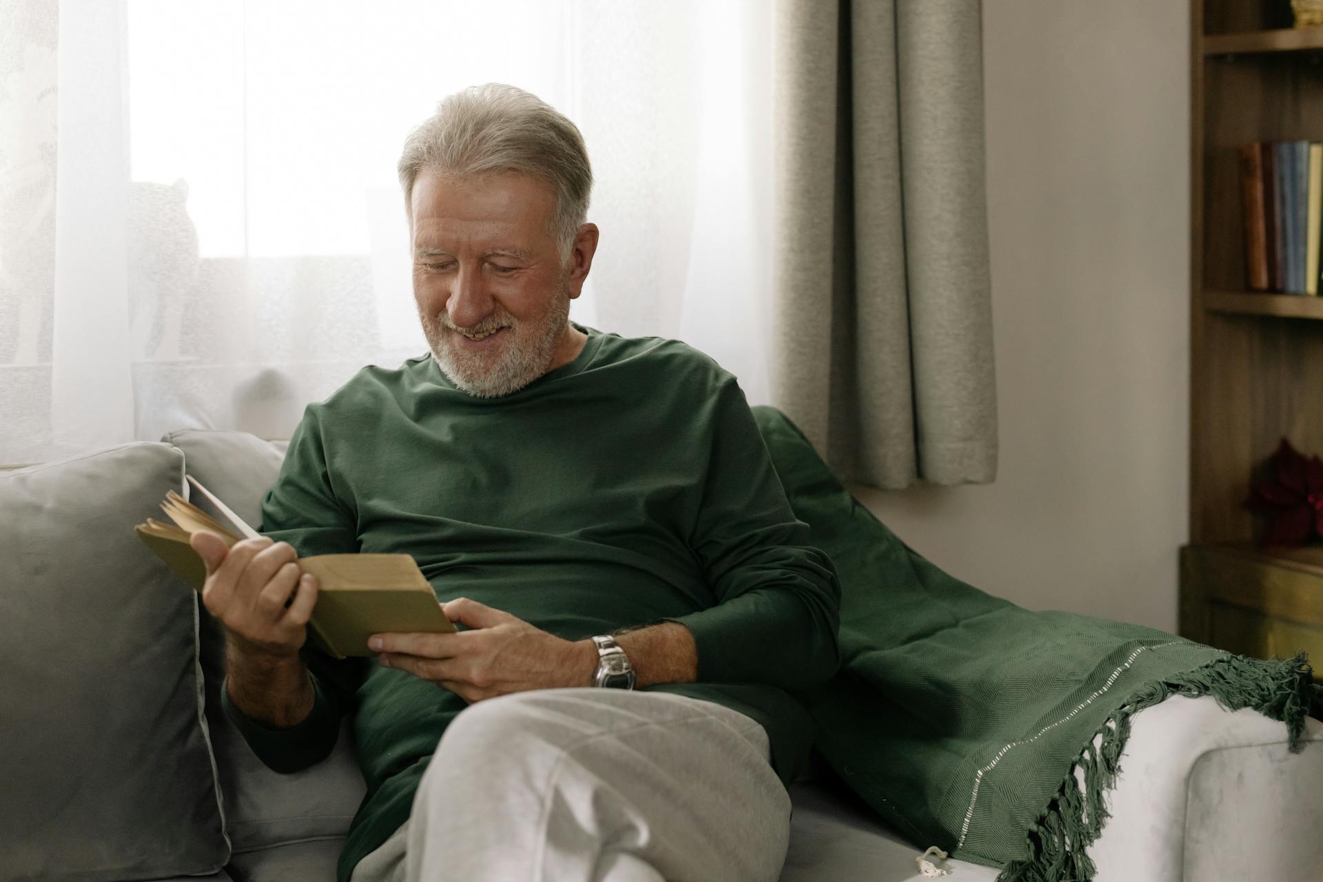 Un anciano sonriente leyendo un libro | Fuente: Pexels