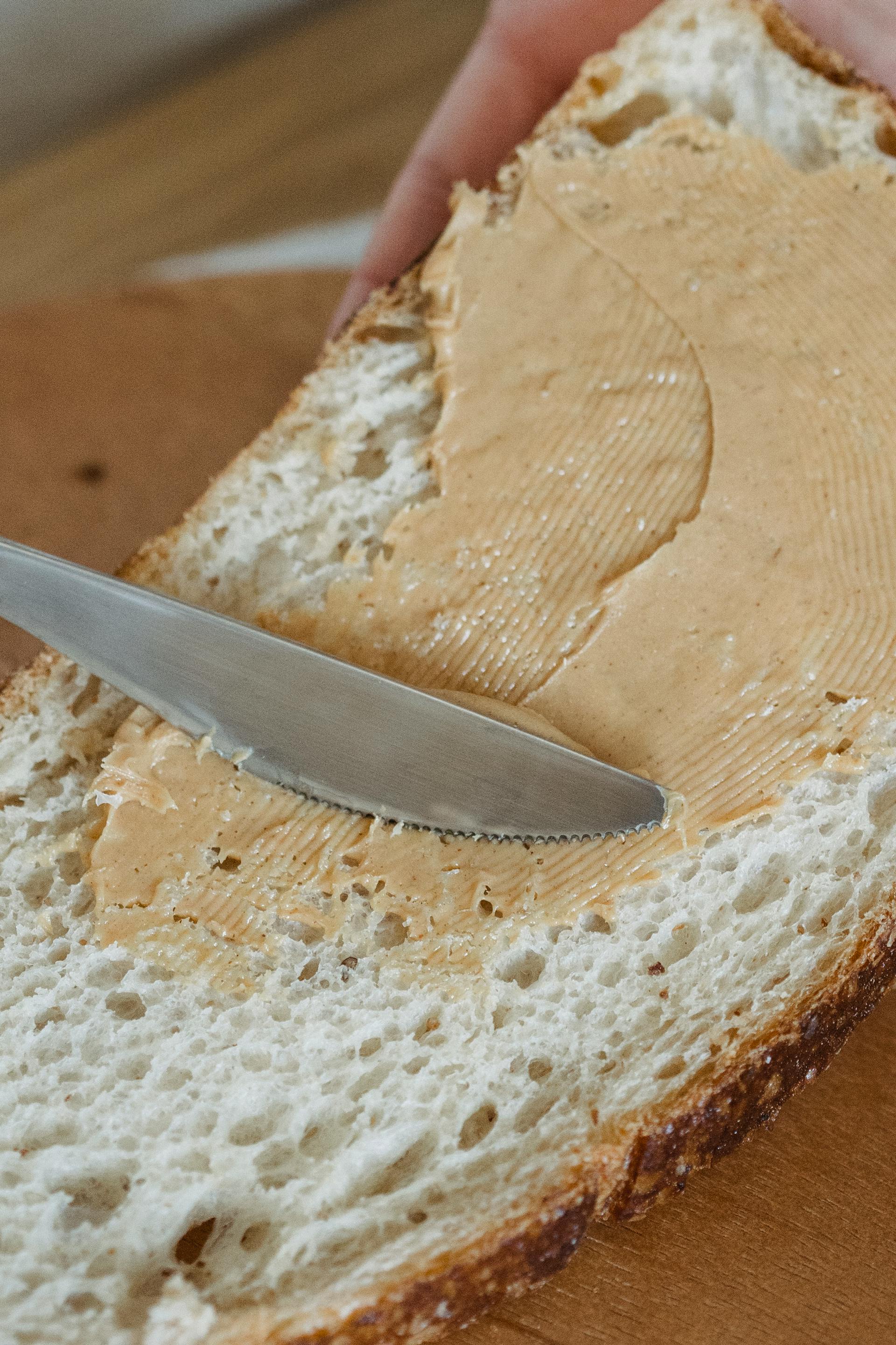 Una persona poniendo mantequilla de maní en una rebanada de pan | Fuente: Pexels