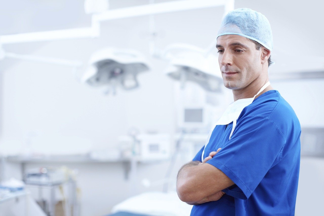 Un médico vestido con una bata azul con las manos cruzadas en un hospital. | Foto: Pixabay / Free-Photos
