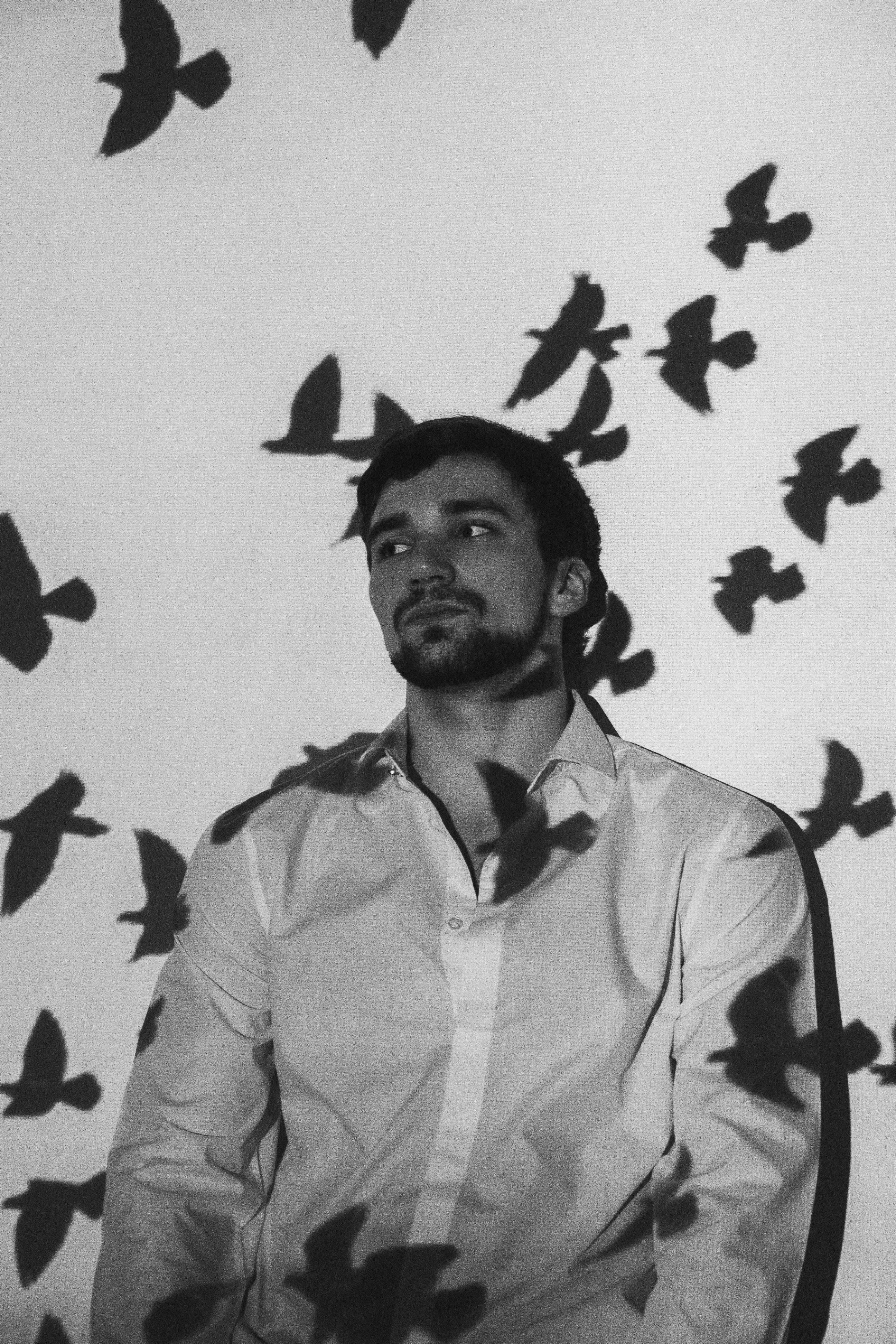 Hombre pensativo cerca de la pared con sombras de pájaros | Foto: Pexels