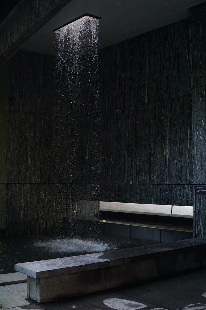 Ducha tipo cascada en un cuarto de baño con baldosas oscuras y banquillo. | Foto: Unsplash