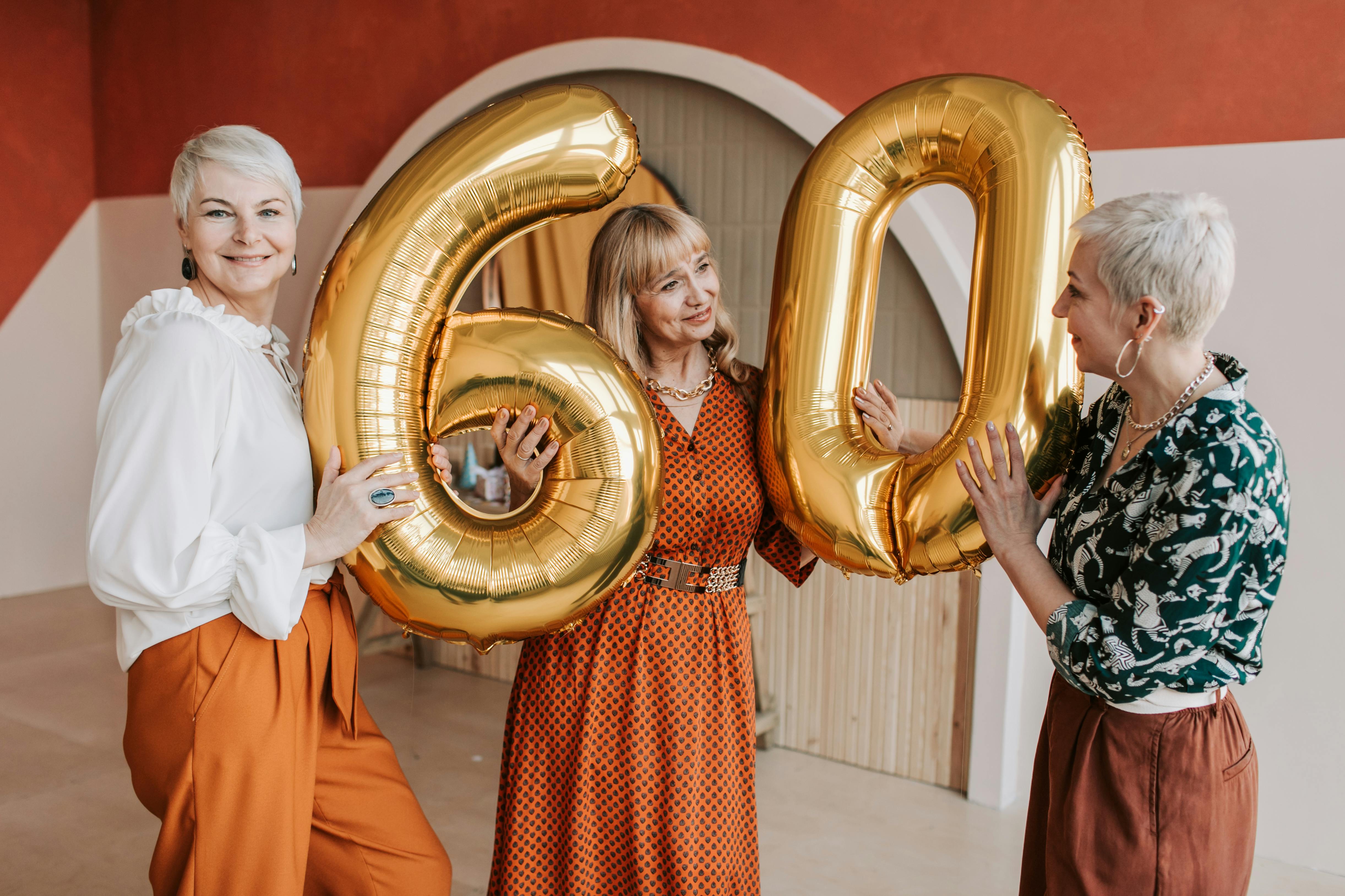 Tres mujeres sostienen globos de cumpleaños en los que está escrito el número "60" | Fuente: Pexels