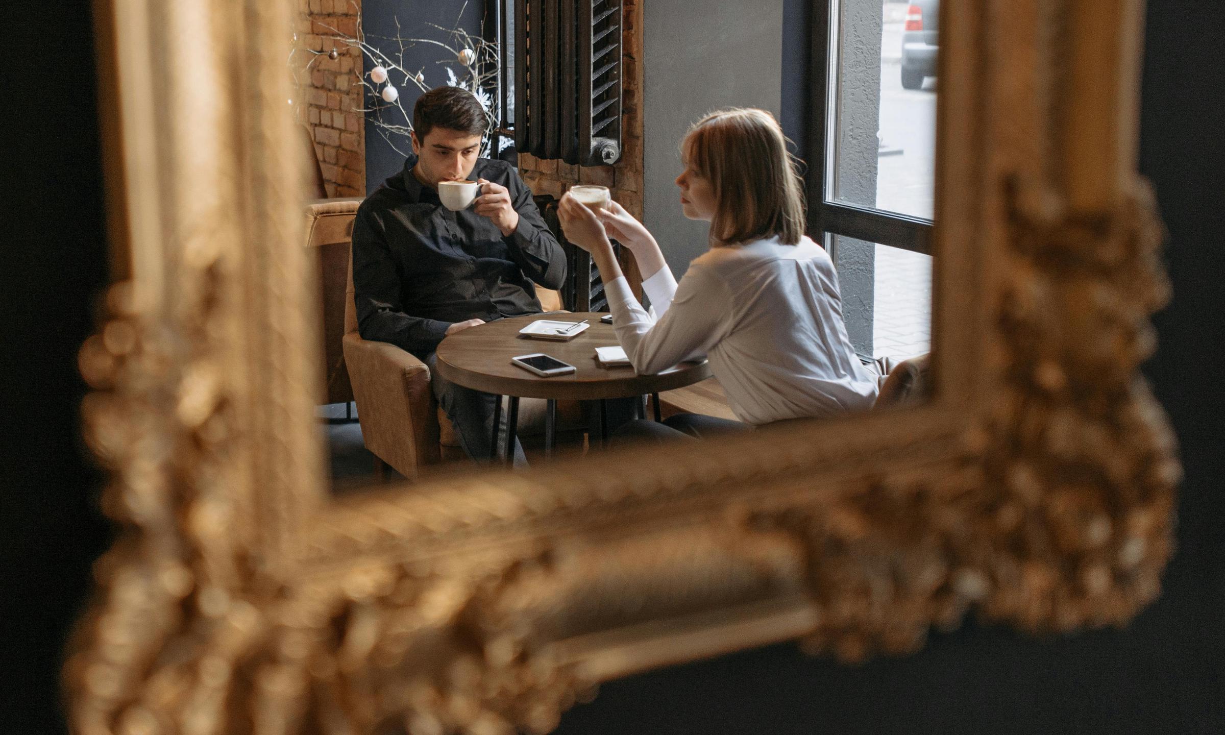 Un hombre y una mujer reflejados en el espejo de una cafetería | Fuente: Pexels