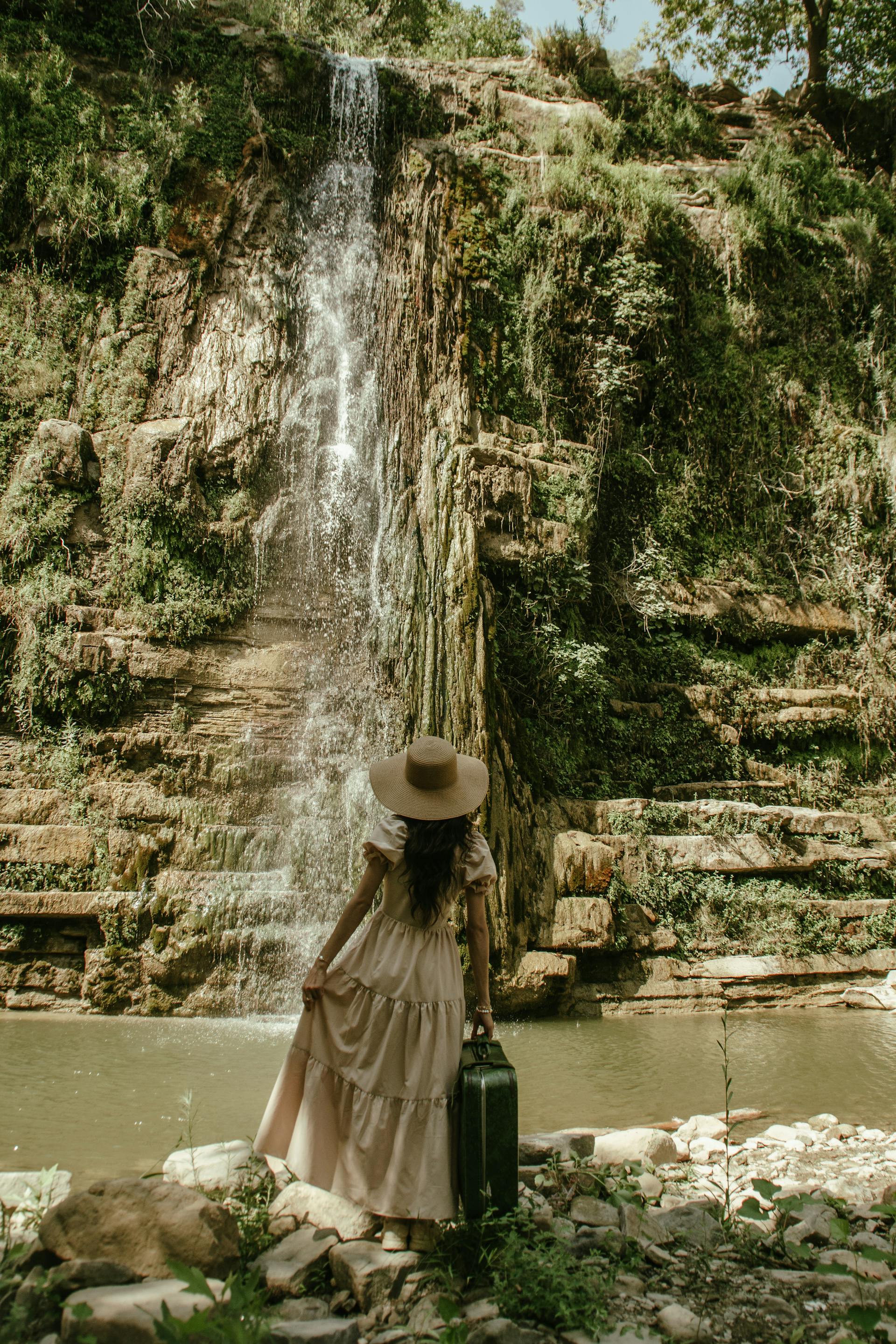 Una mujer con vestido beige y sombrero de paja mirando una cascada | Fuente: Pexels