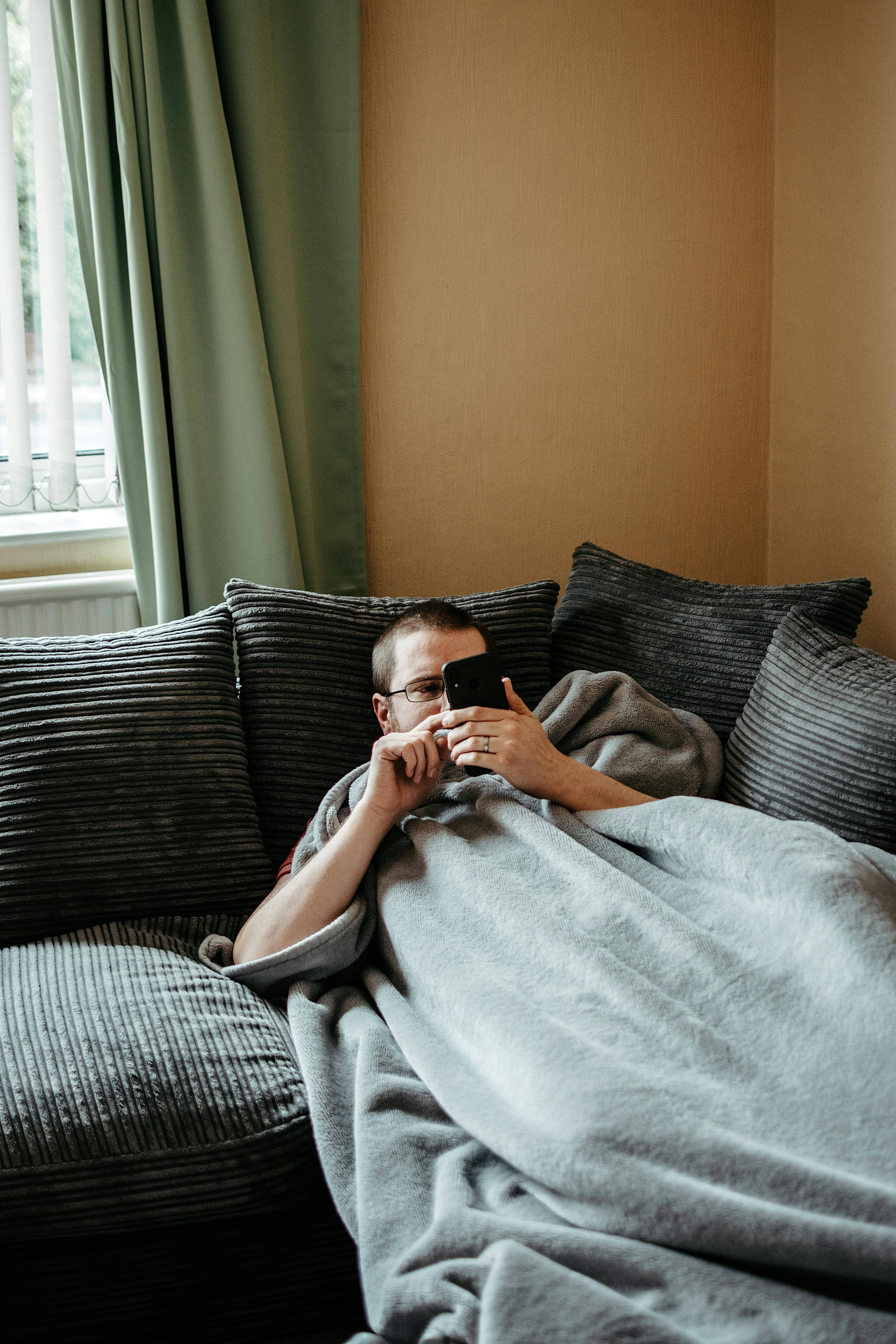 Un hombre holgazaneando en un sofá mientras usa su teléfono | Fuente: Pexels