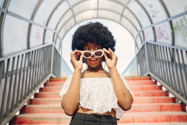 Mujer con afro sosteniendo lentes de sol. │Foto: Freepik
