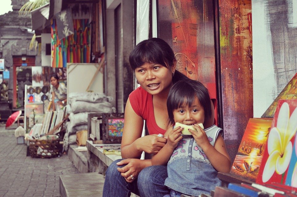 Madre junto a su hija mientras come frutas en mercado de artesanía. | Foto: Max Pixel