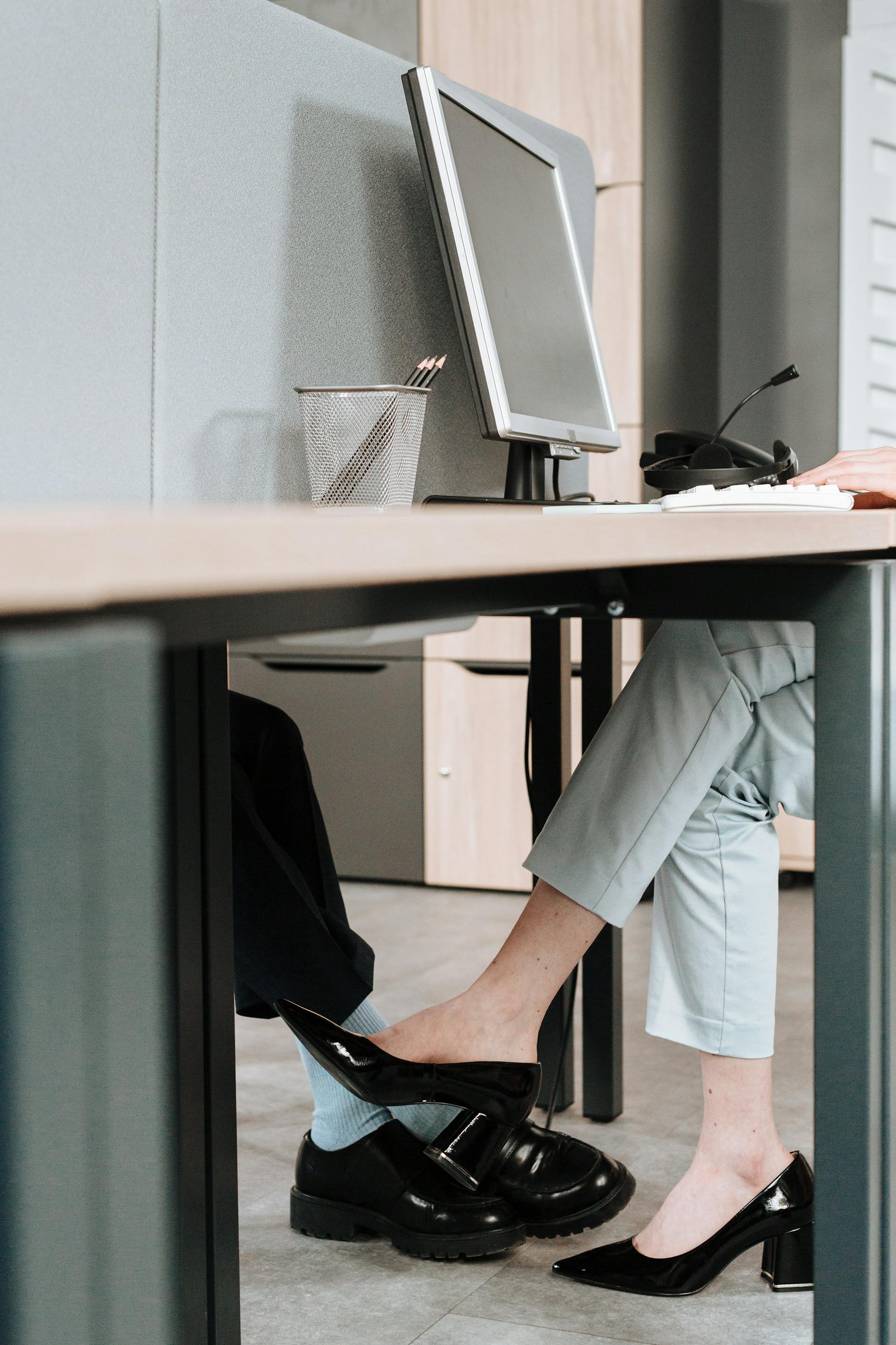Un primer plano de compañeros coqueteando bajo el escritorio | Fuente: Pexels