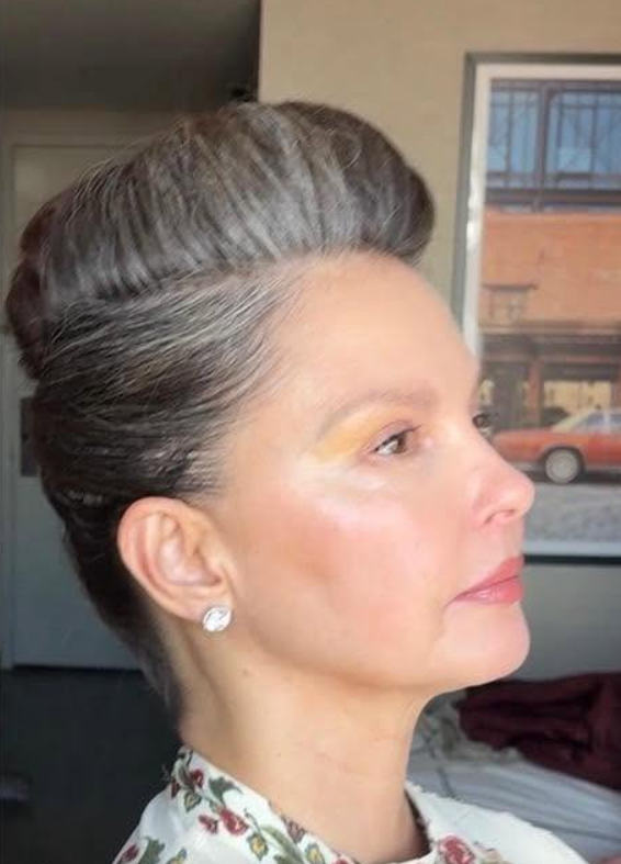 Ashley Judd luce su melena con mechas plateadas en un elegante recogido en una foto de 2025. El perfil lateral resalta el contraste entre sus raíces grises y el resto del pelo, más oscuro. | Fuente: Facebook/AshleyJuddOfficial