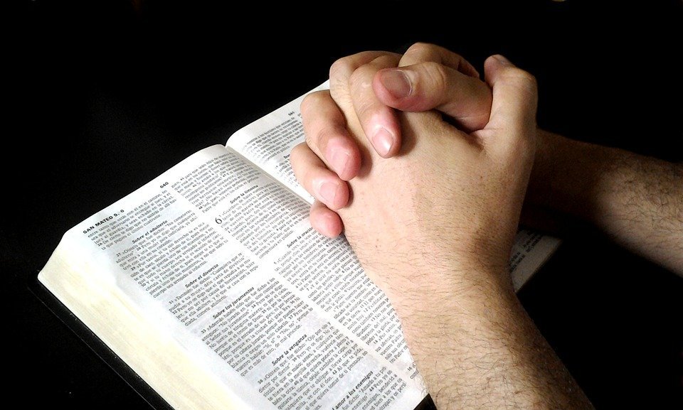 Persona rezando junto a la biblia. | Foto: Pixabay