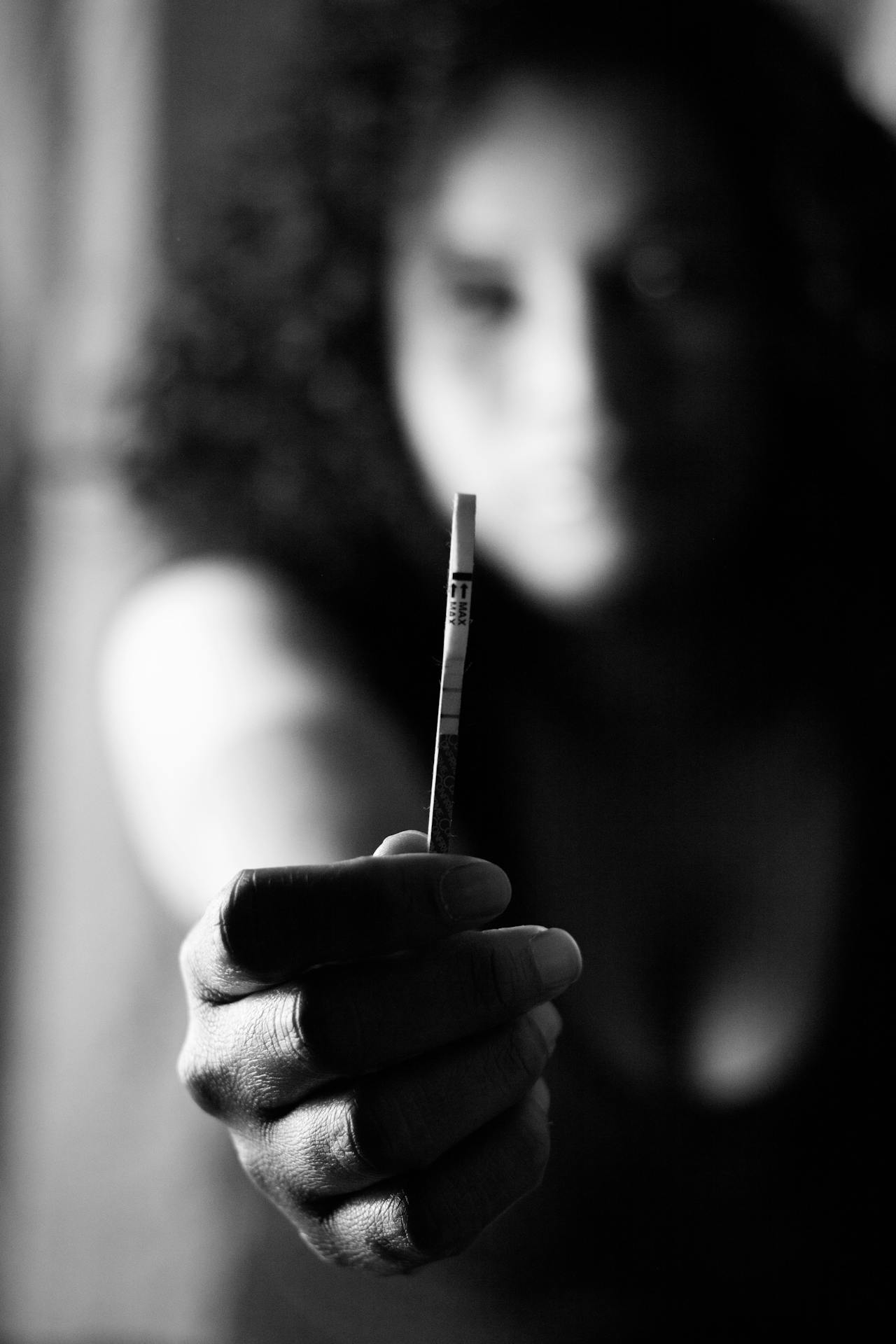 Toma en escala de grises de una mujer que sostiene una prueba de embarazo enfocada | Fuente: Pexels
