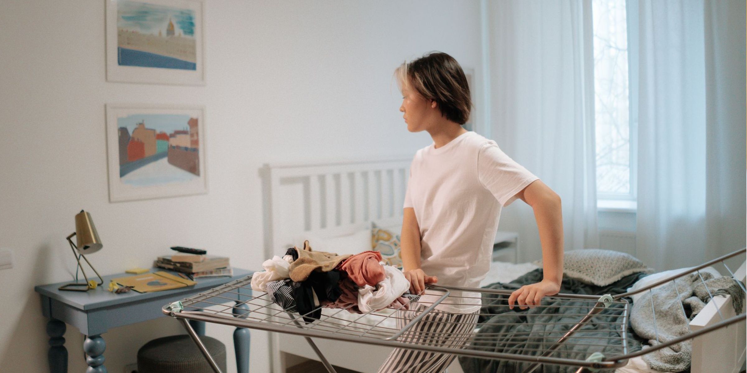 Una chica está de pie en un dormitorio muy chulo, ordenando la ropa en un tendedero | Fuente: Pexels