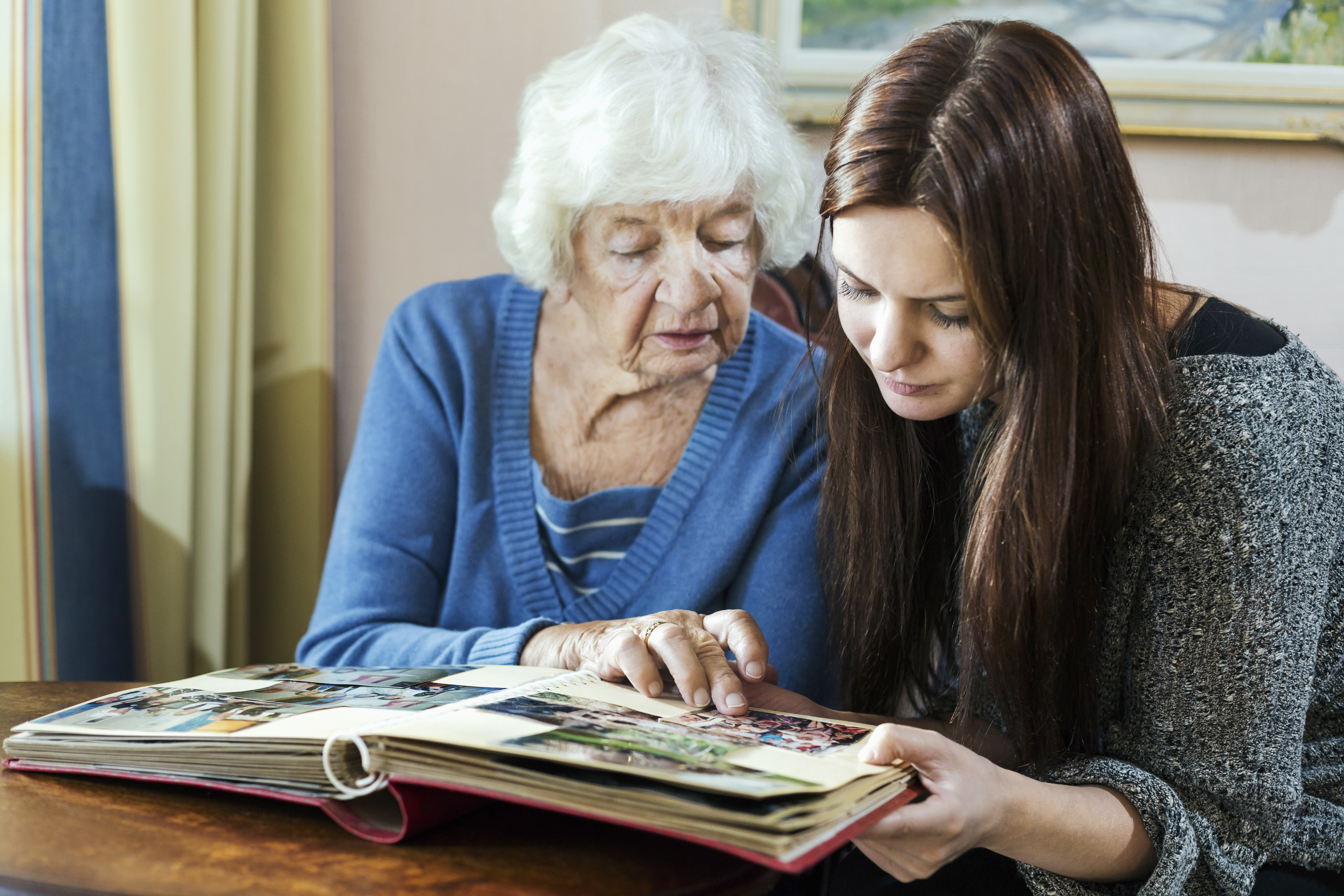 Abuela y nieta mirando un álbum de fotos en casa | Foto: Getty Images