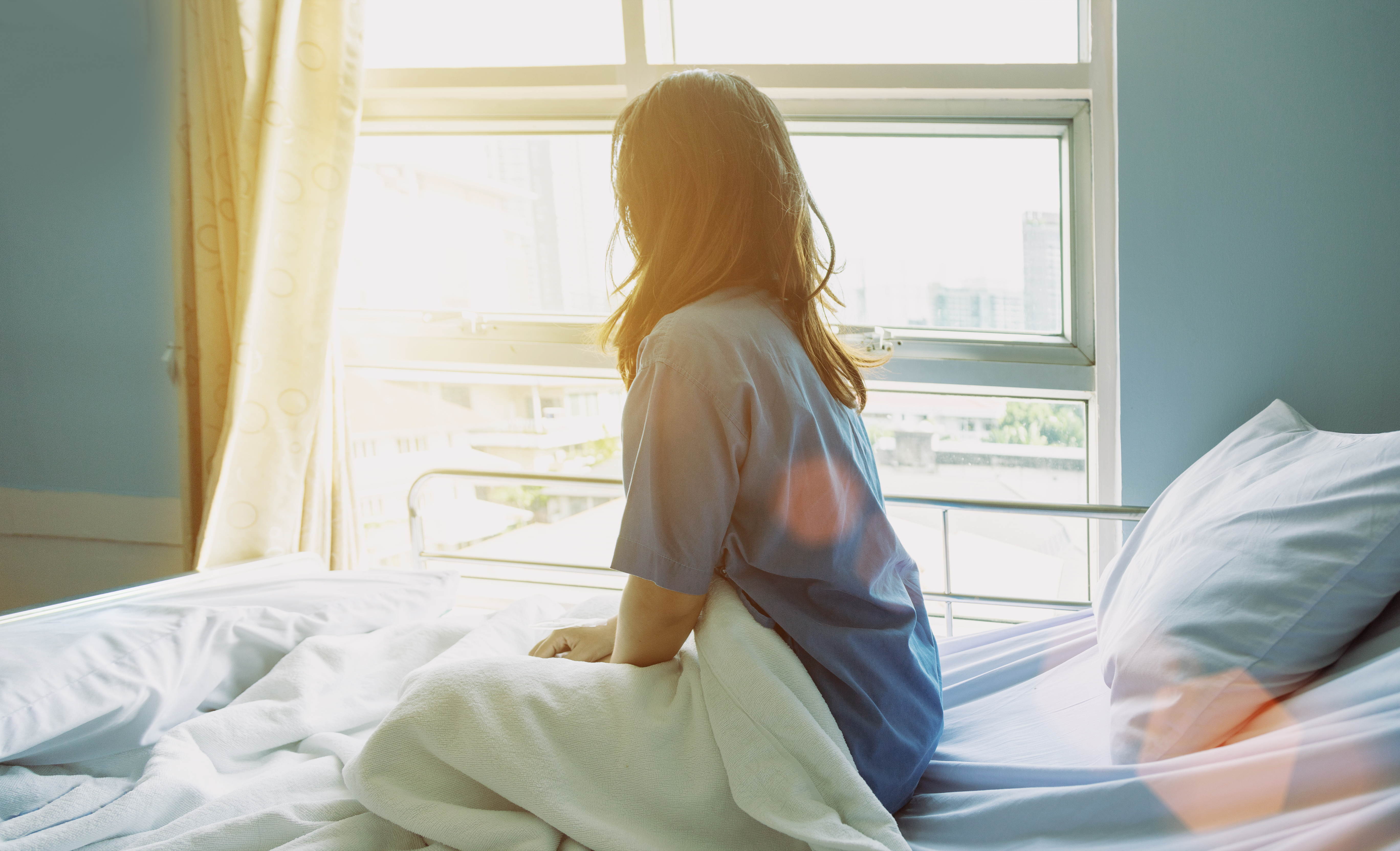 Una mujer mira por la ventana sentada en la cama de un hospital | Foto: Shutterstock
